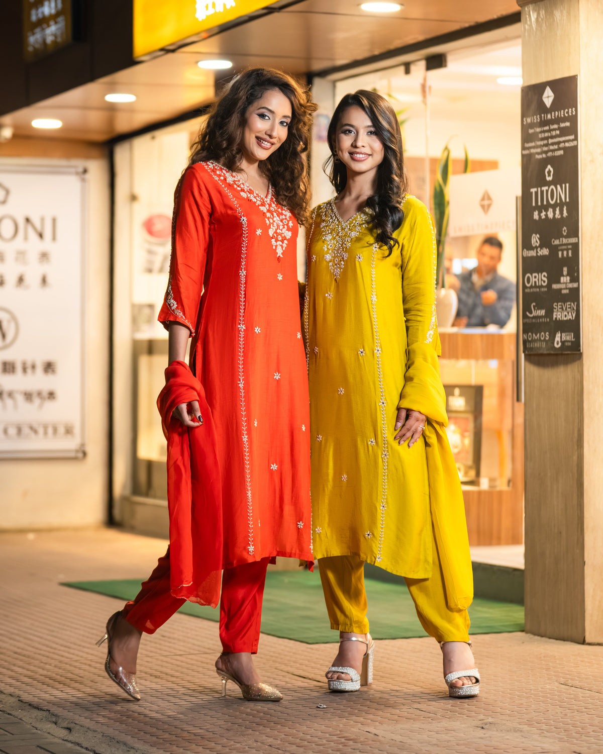 Two women in colorful traditional outfits standing in front of a store entrance.