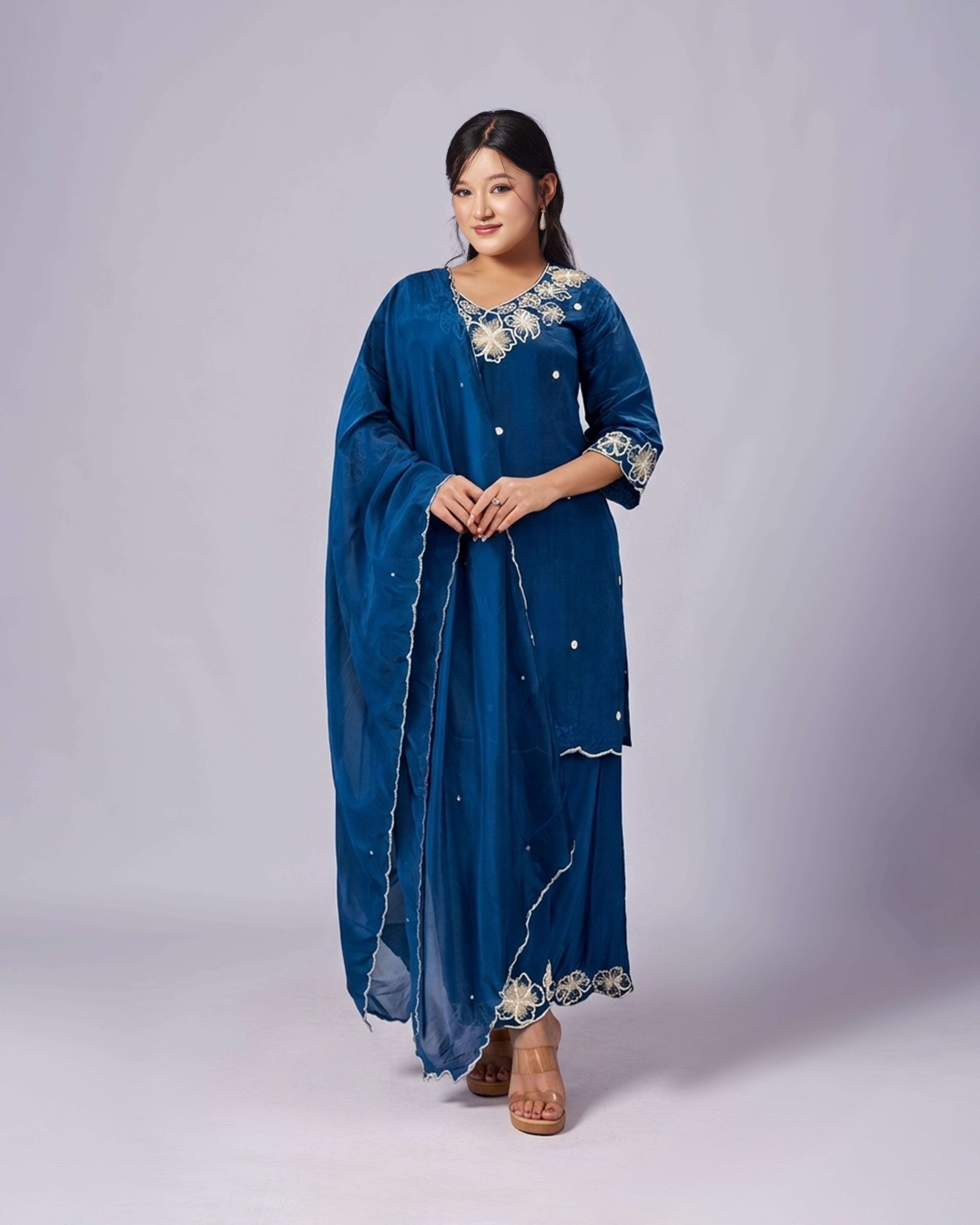 Woman wearing a blue traditional outfit with intricate designs on a plain background