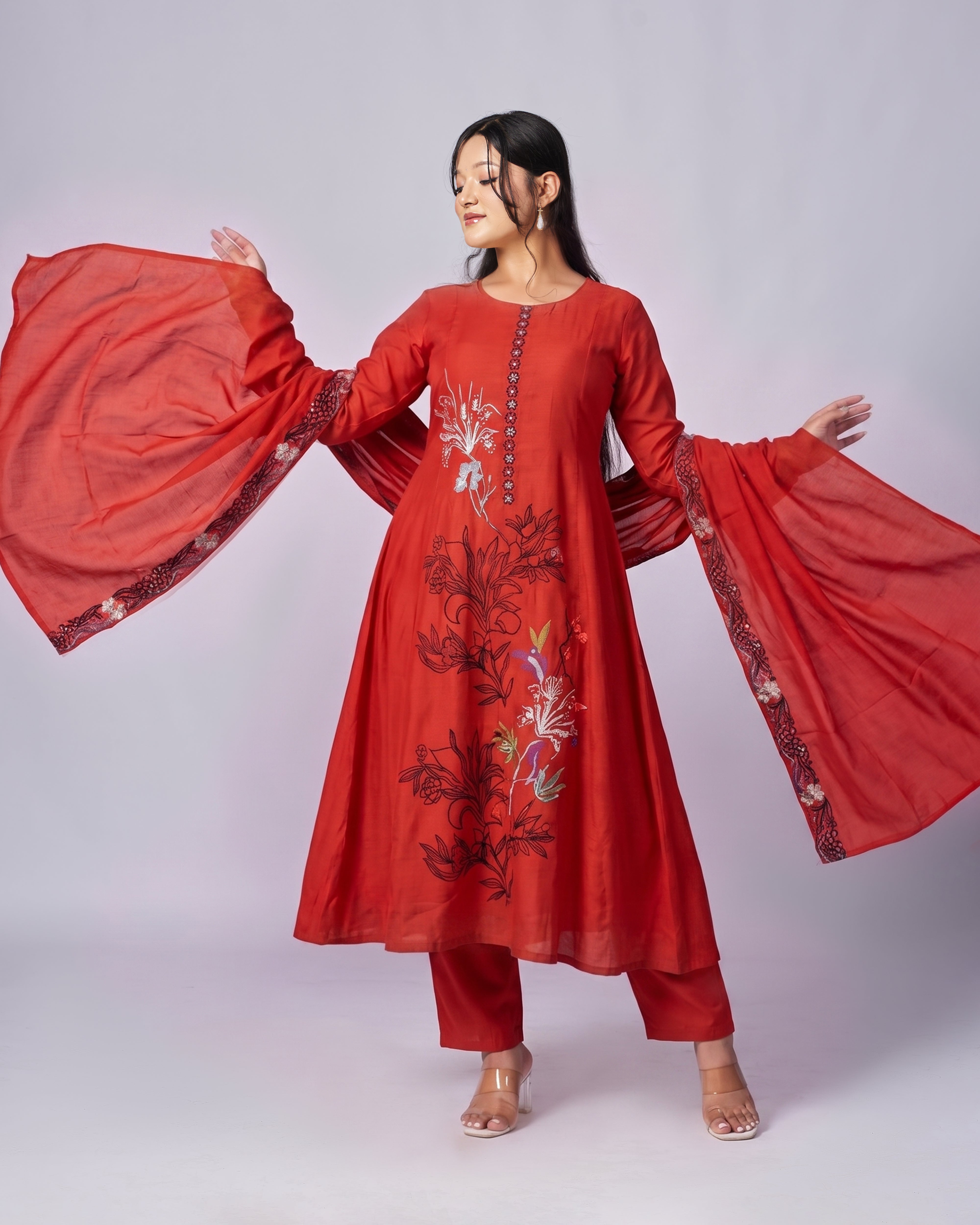 Woman wearing a red embroidered traditional outfit with a flowing scarf on a white background