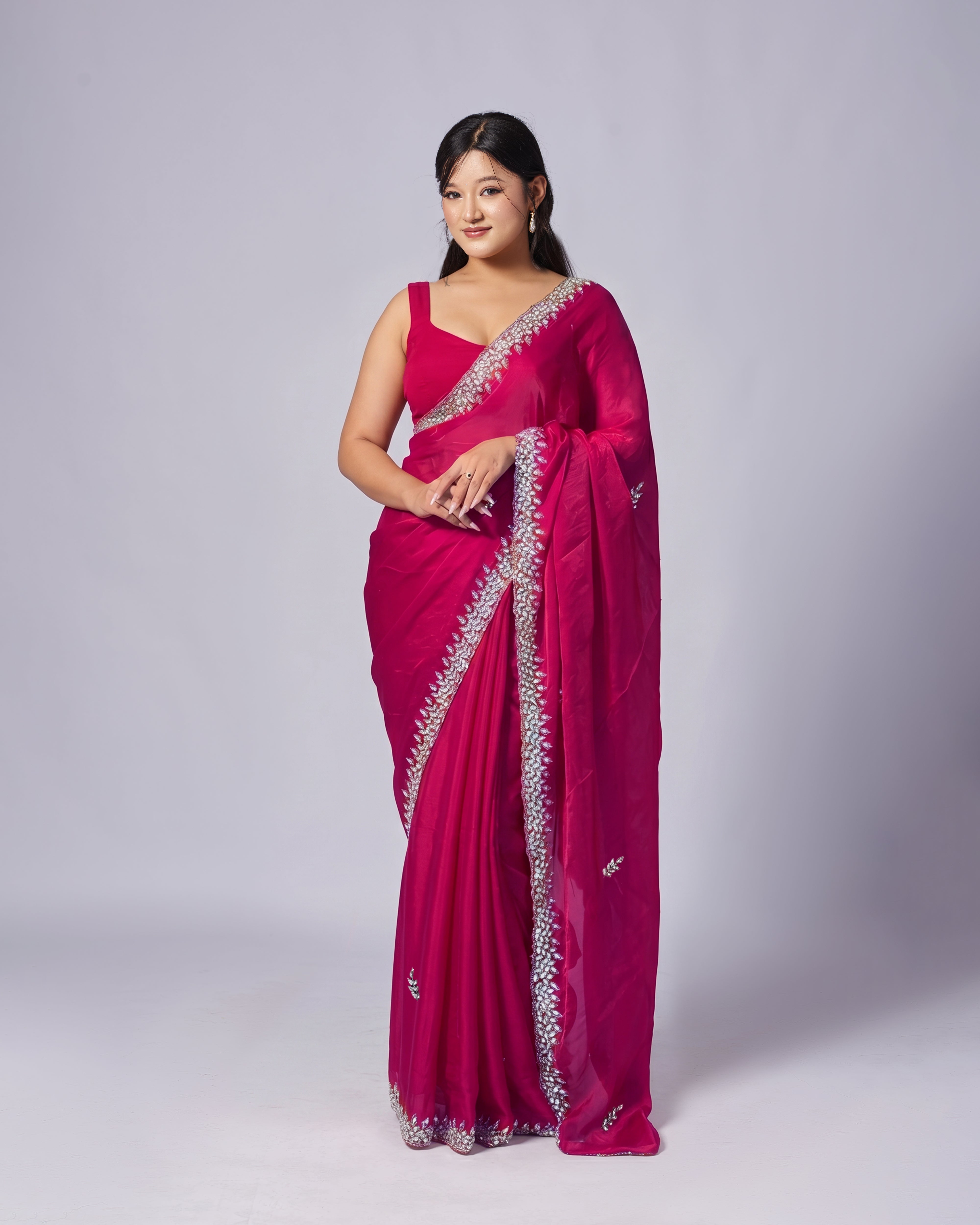 Woman wearing a vibrant pink saree with silver border on a plain background