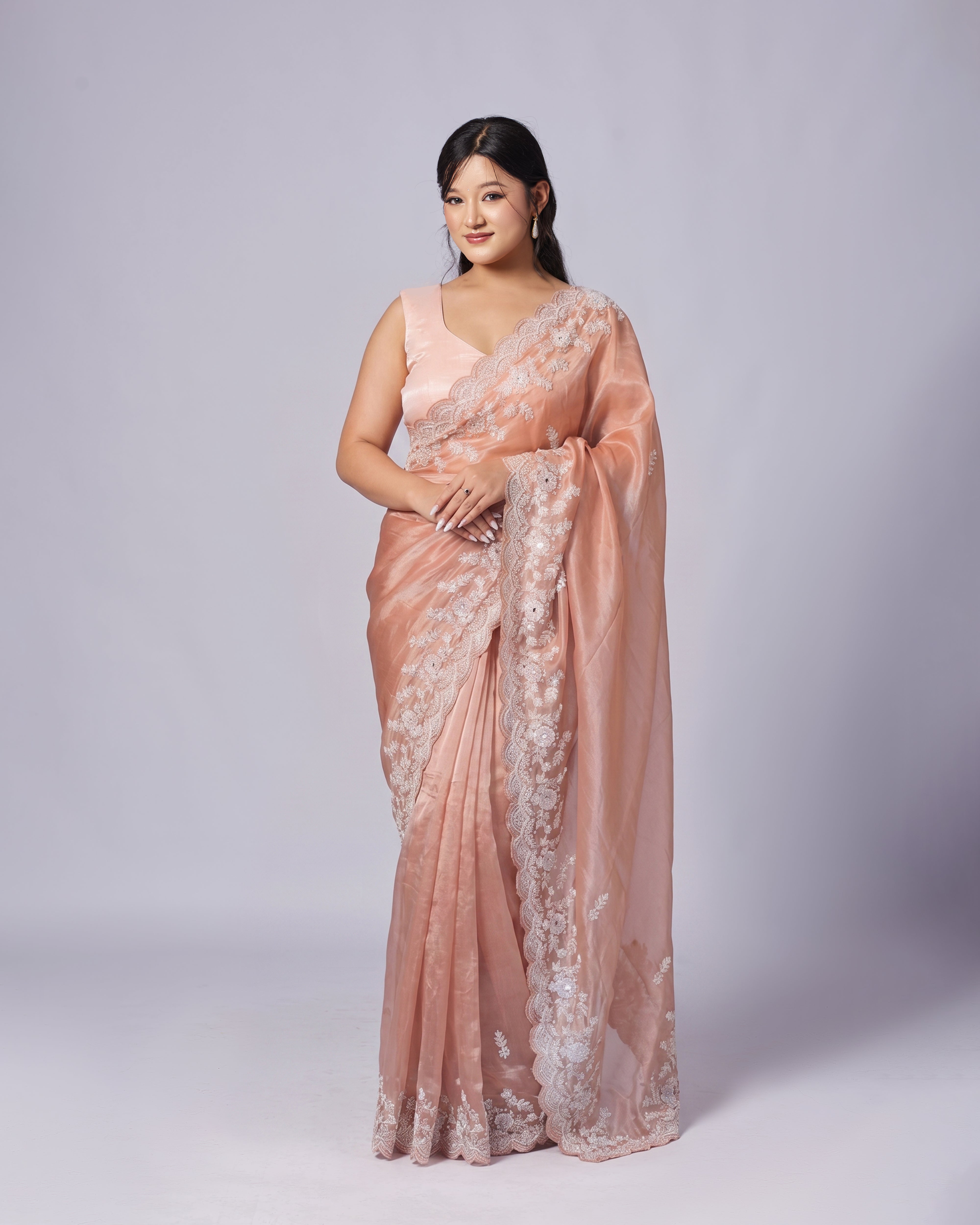 Woman wearing a pink saree with white lace on a light gray background