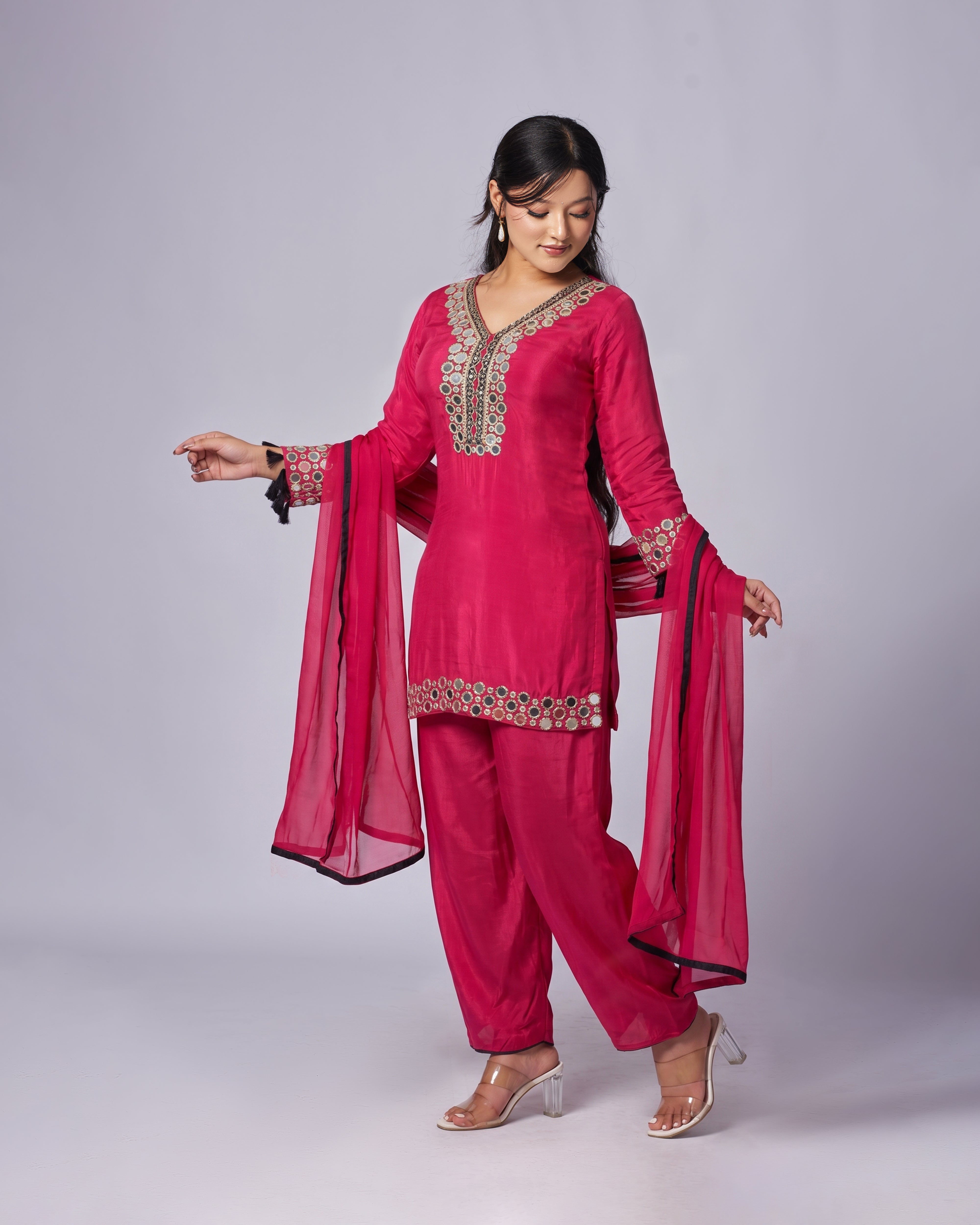 Woman wearing a pink traditional outfit with intricate designs on a gray background 
