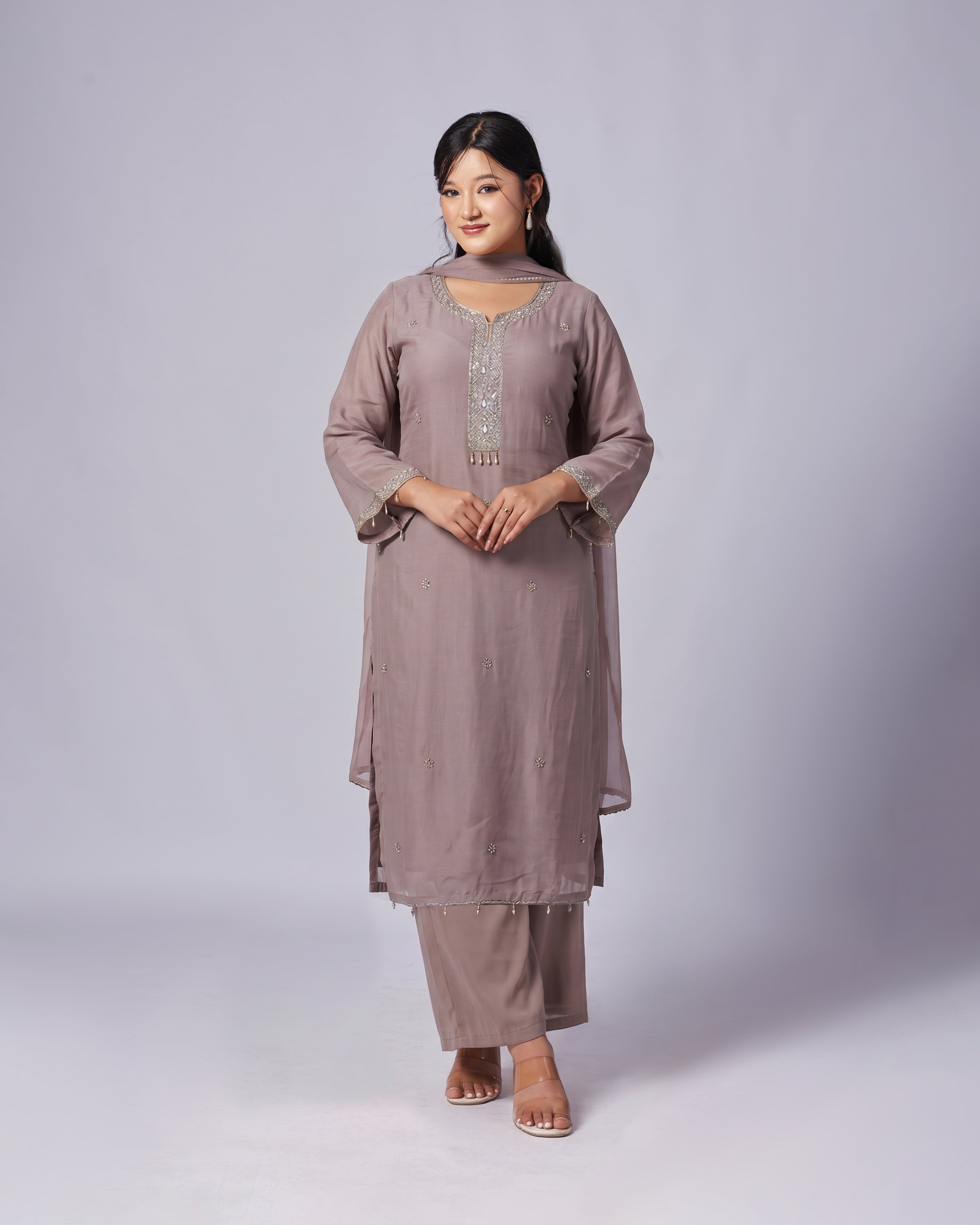 Woman wearing a mauve traditional outfit with intricate detailing on a white background