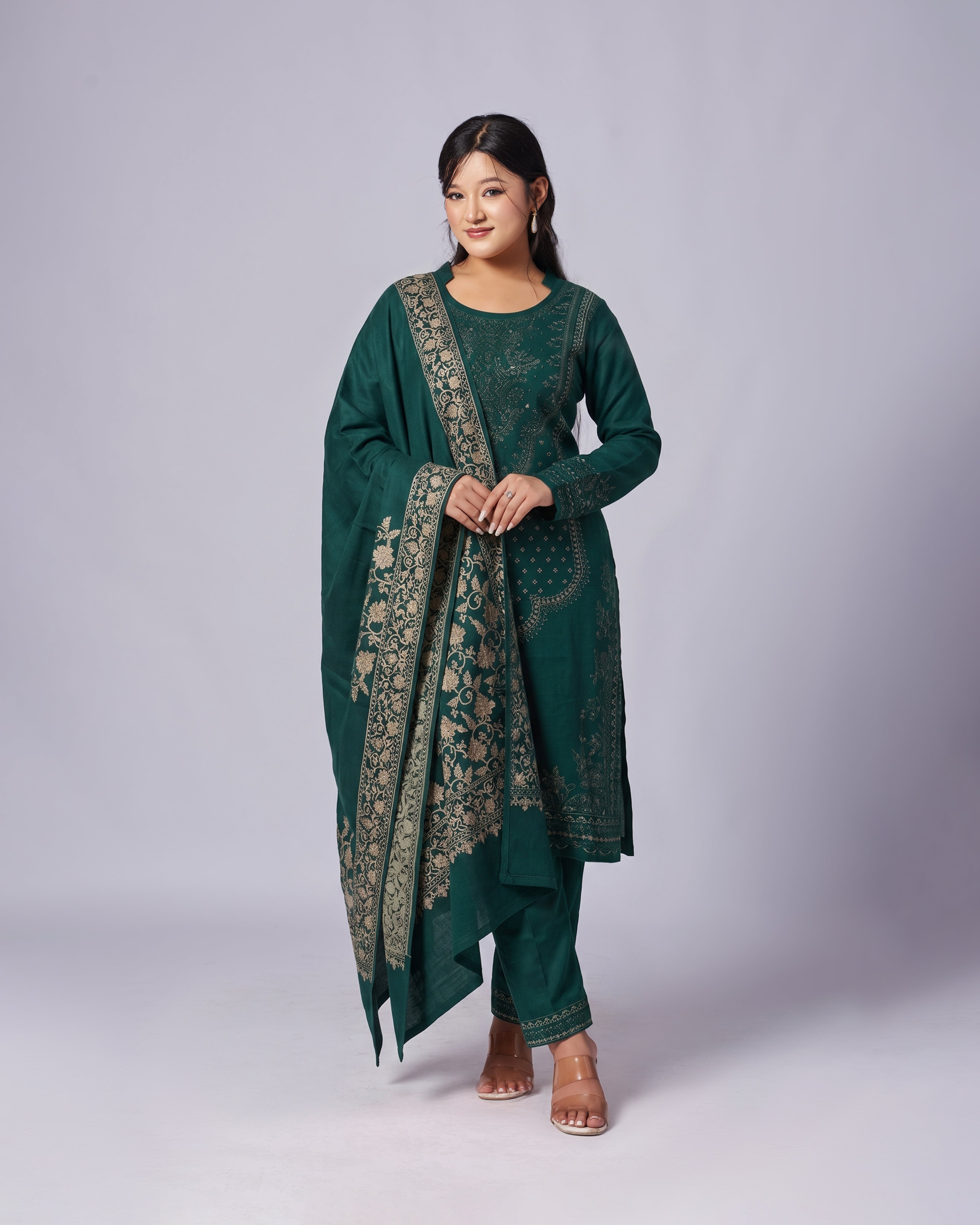Woman wearing a green traditional outfit with intricate patterns on a plain background