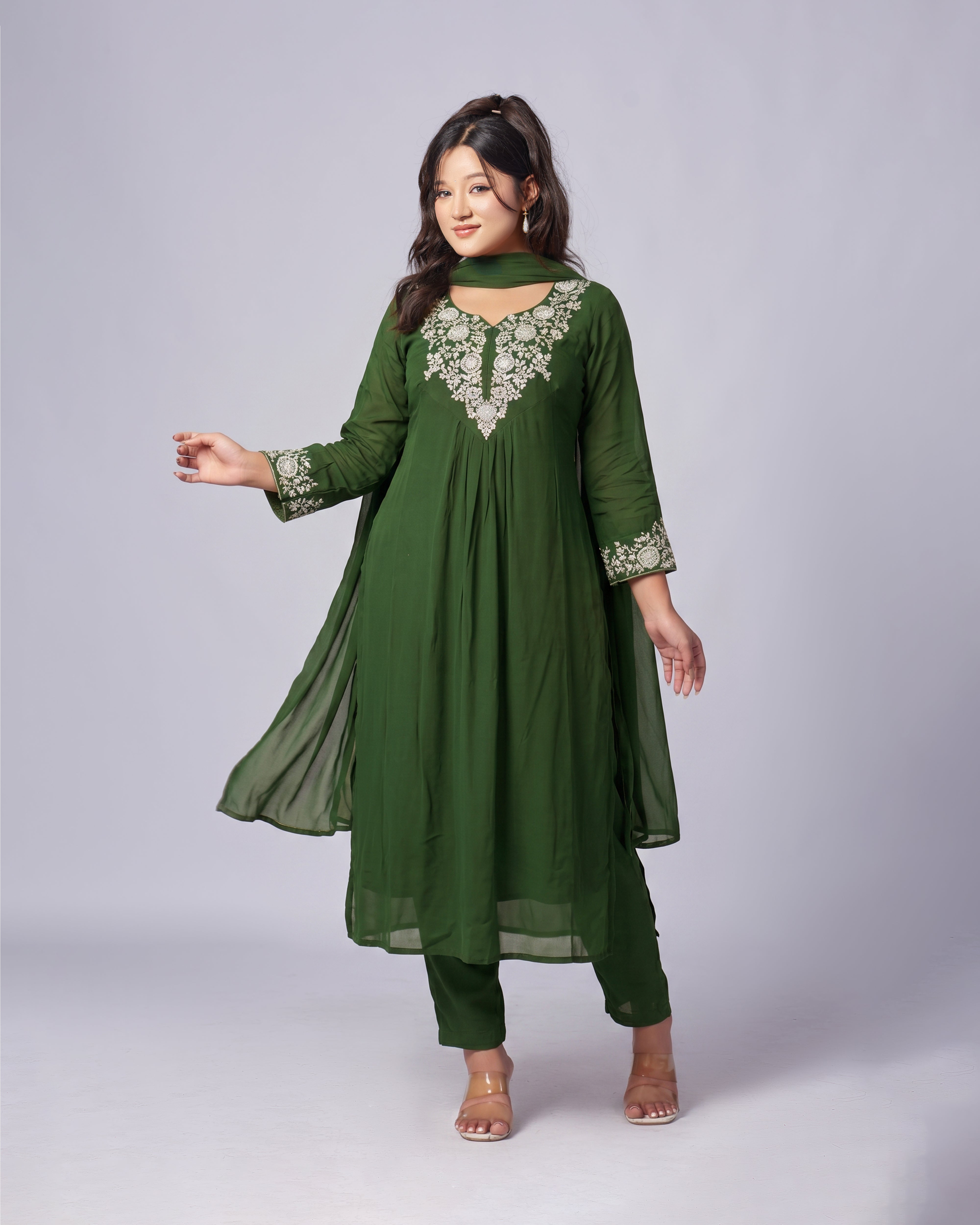 Woman wearing a green traditional outfit with floral embroidery on a light gray background
