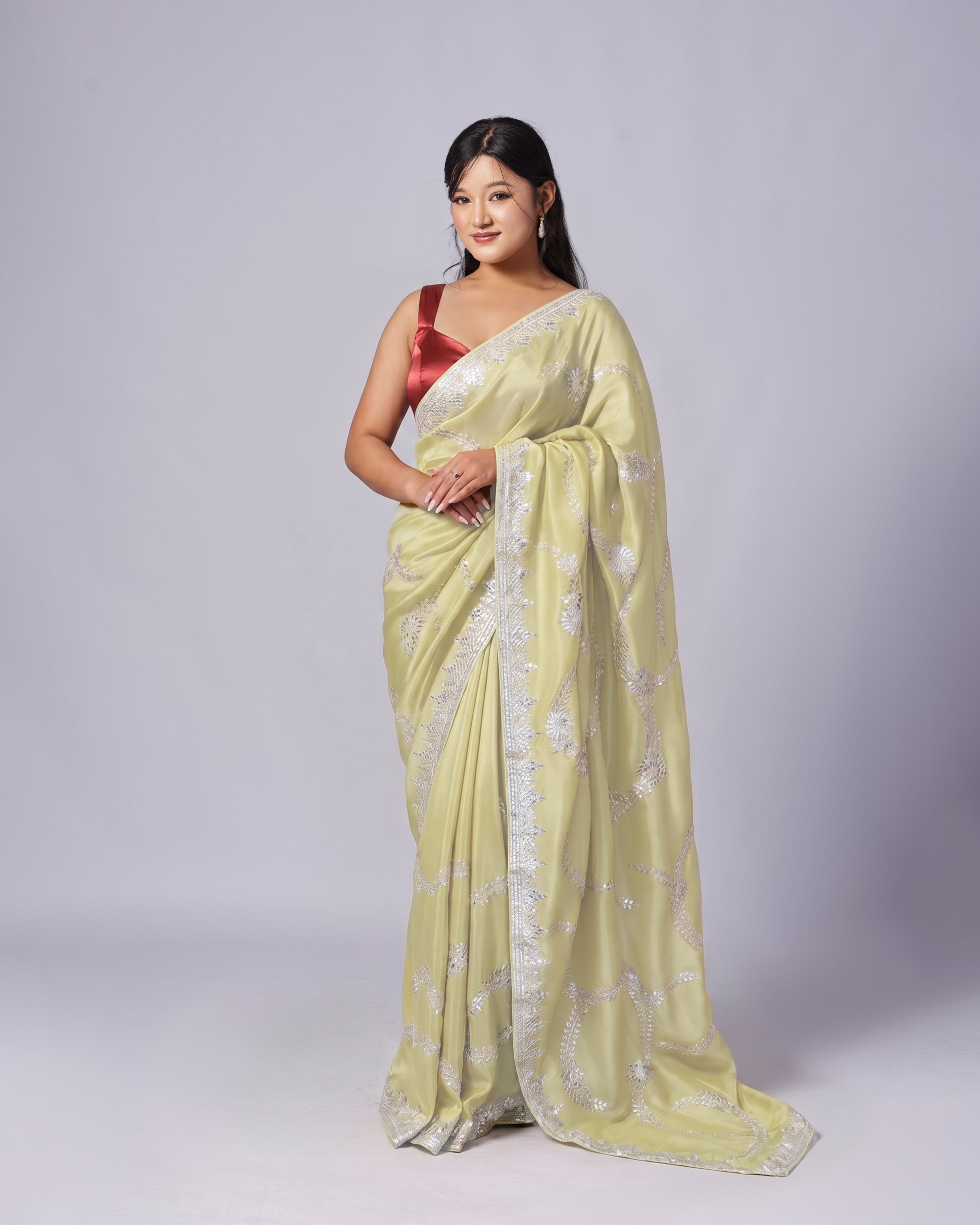 Woman wearing a light green saree with a red blouse against a white background