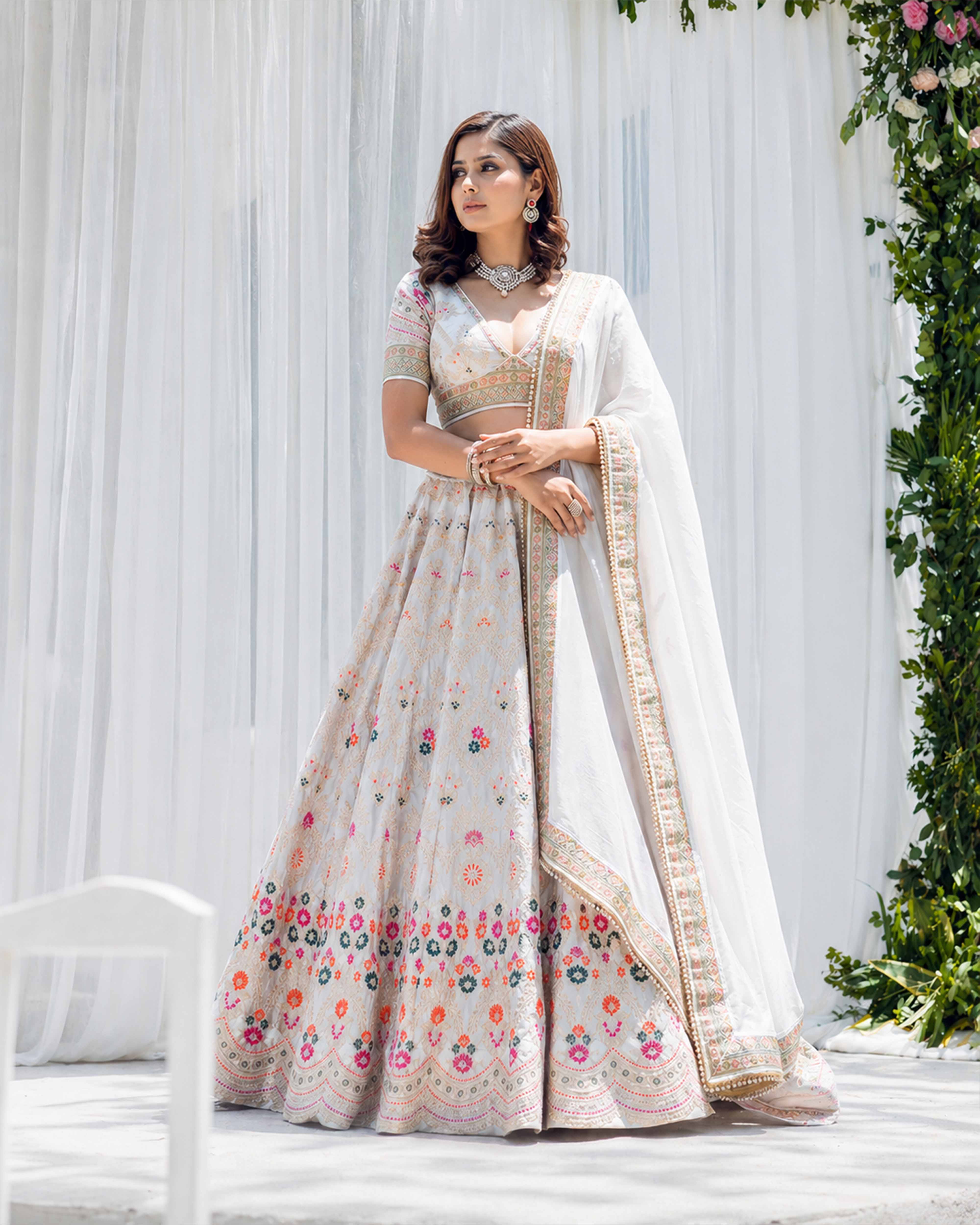 Woman in a floral saree standing against a white curtain with greenery