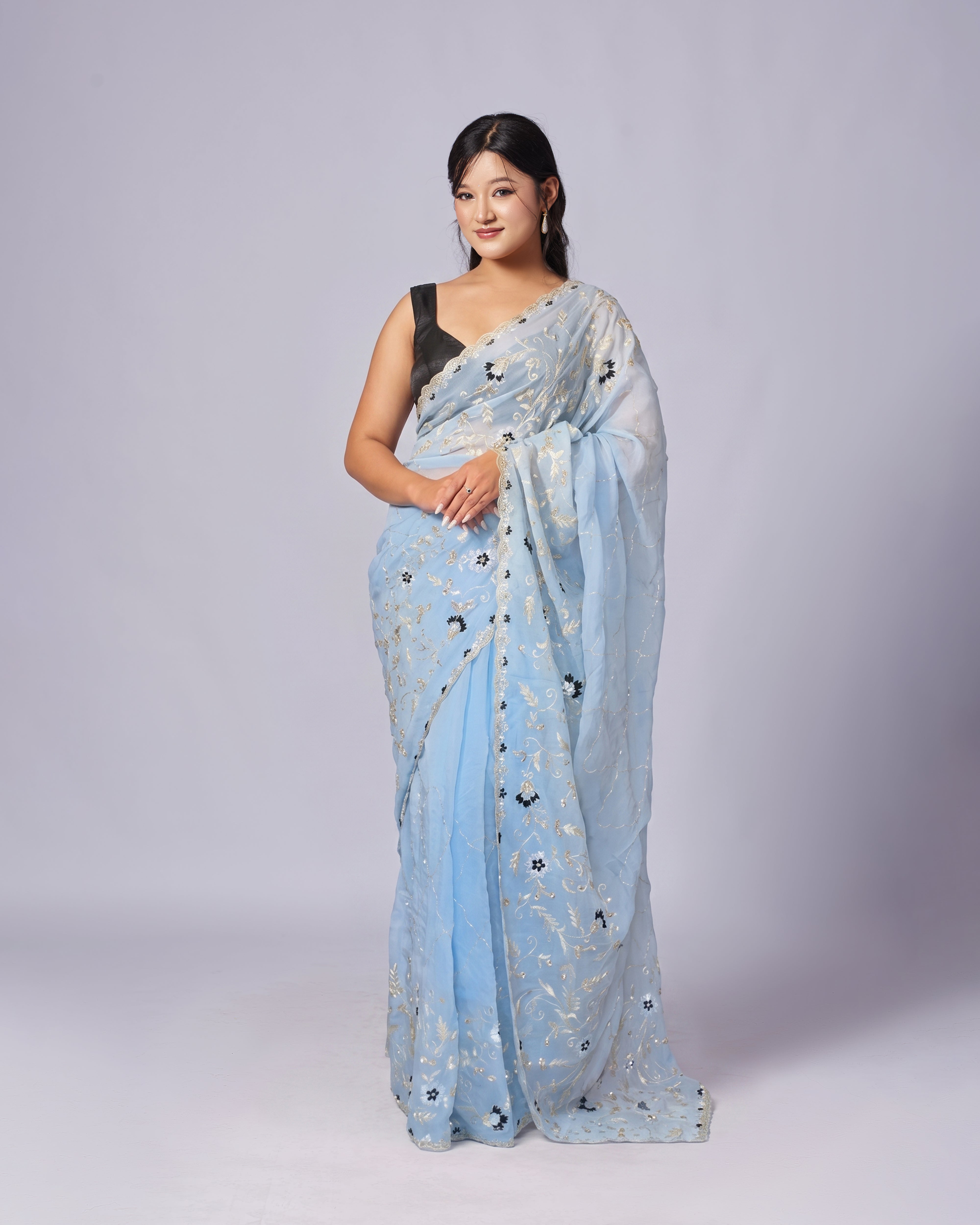 Woman wearing a light blue saree with floral patterns on a plain background