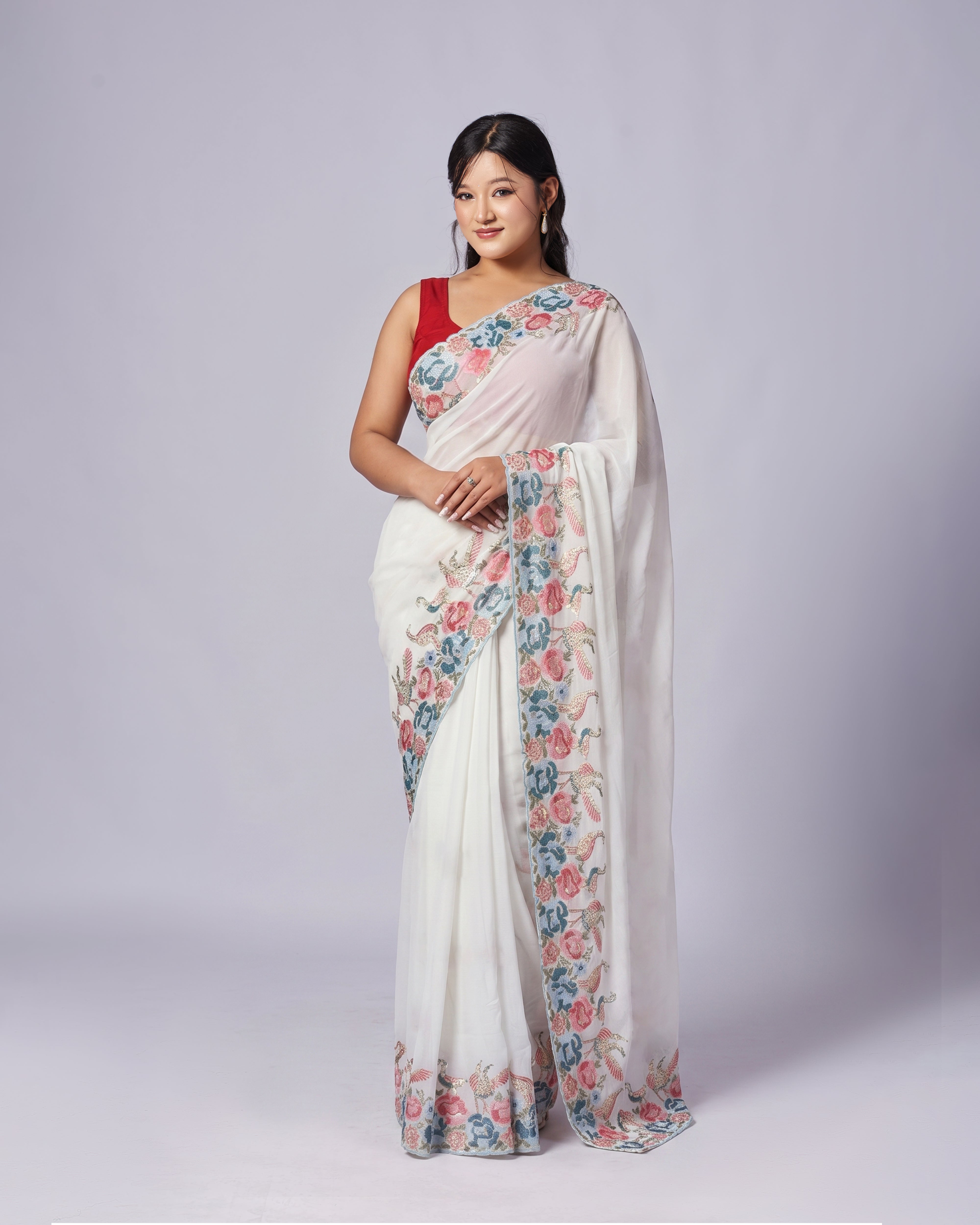 Woman wearing a white saree with floral patterns on a plain background