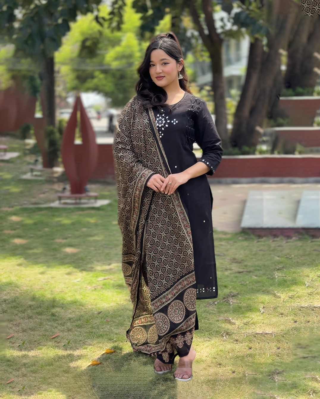 Woman in traditional attire standing outdoors with greenery in the background
