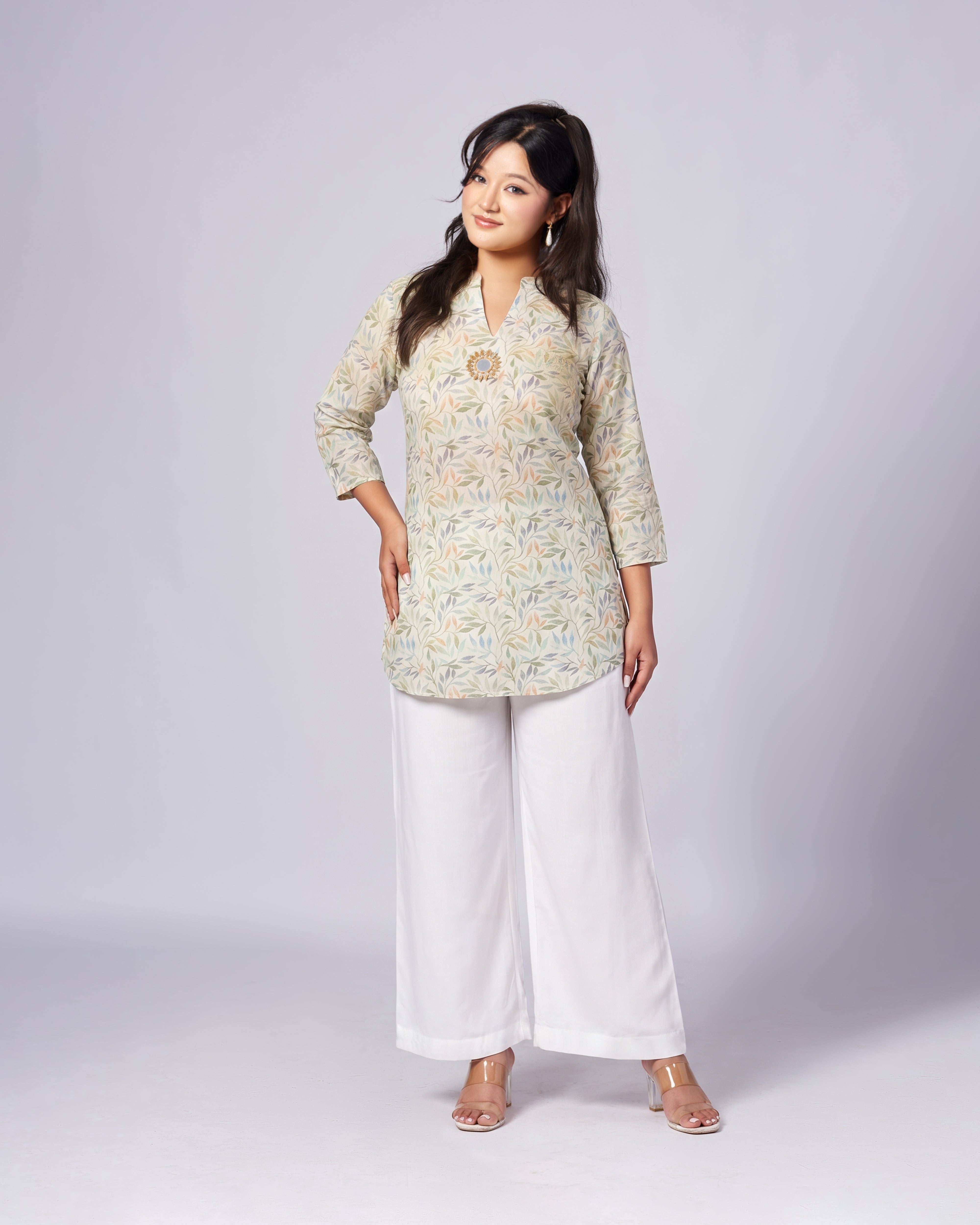 A woman modeling a three-quarter sleeve kurta with a gray and beige abstract pattern, paired with white wide-leg pants, standing against a light gray studio background.