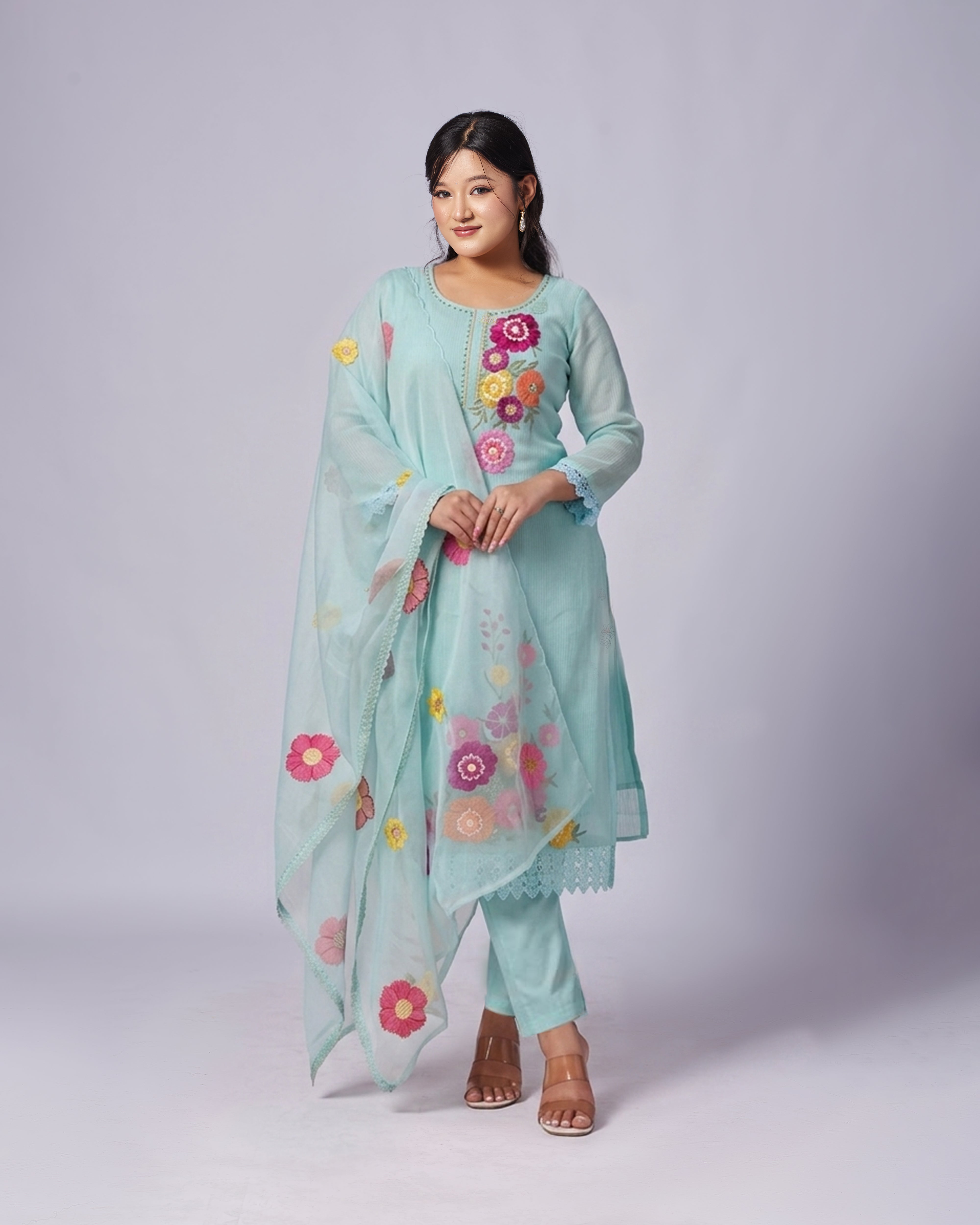 Woman wearing a light blue traditional outfit with floral embroidery on a white background