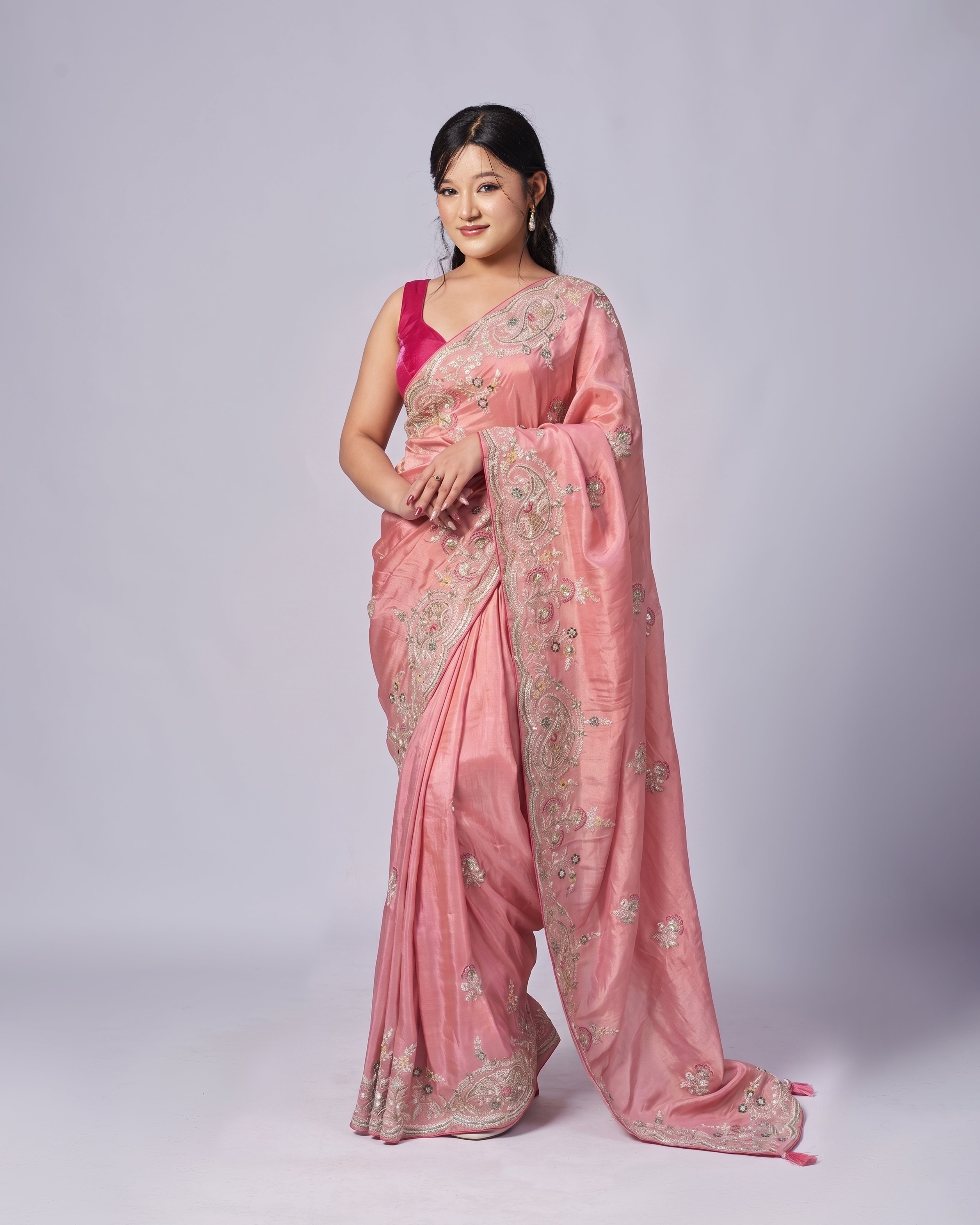 Woman wearing a pink saree with intricate designs on a white background