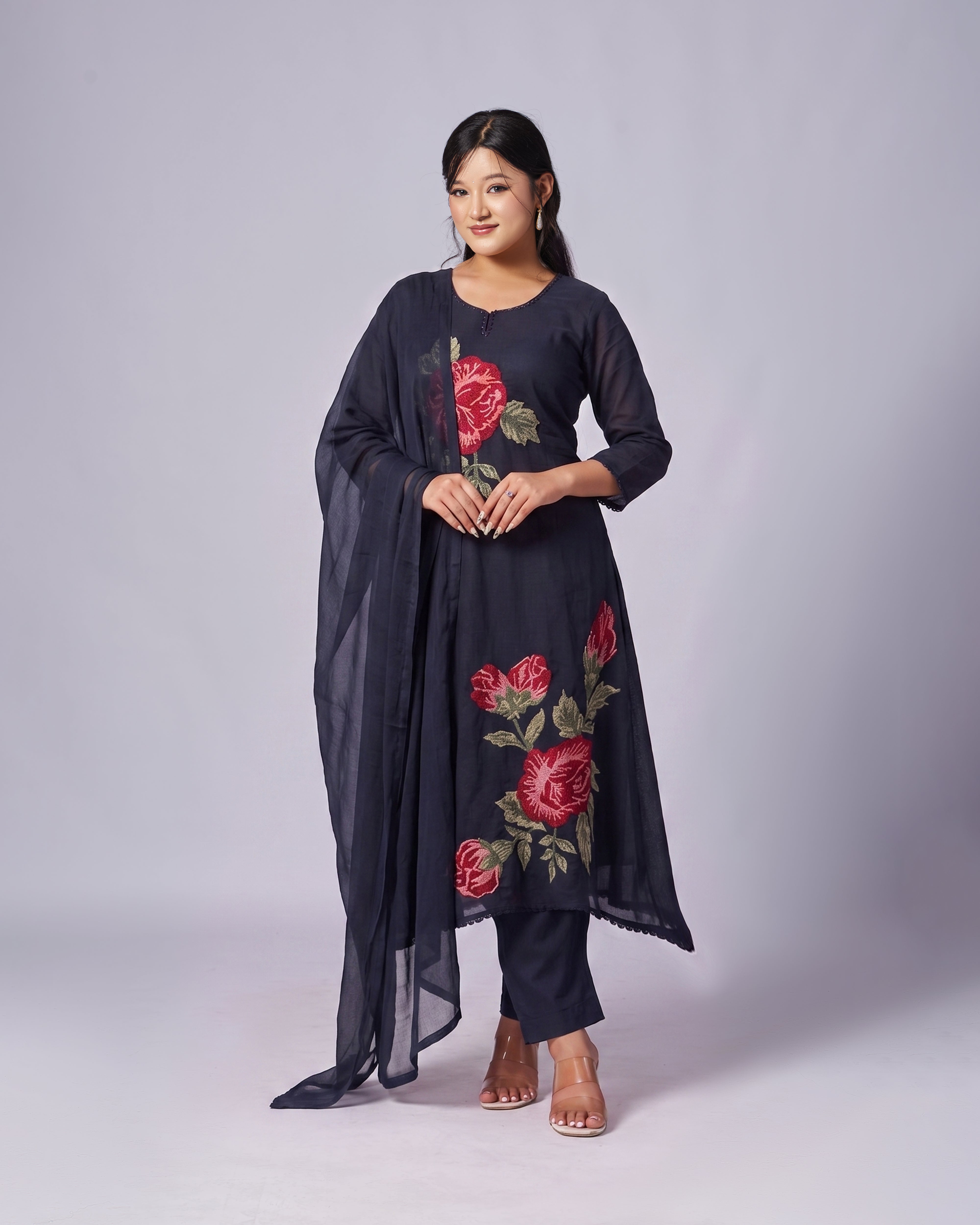 Woman wearing a black outfit with floral embroidery on a plain background