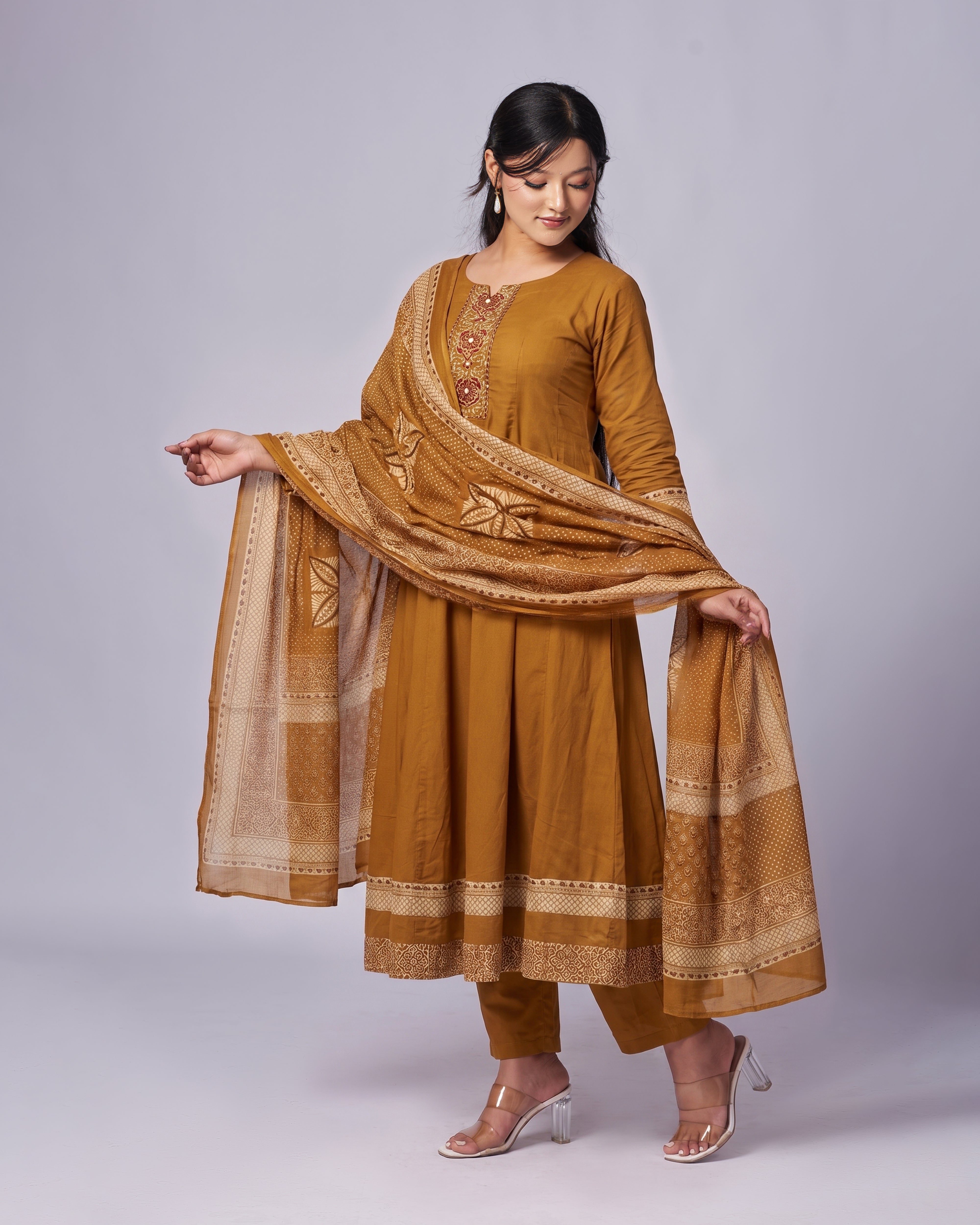Woman wearing a mustard yellow traditional outfit with a matching dupatta on a gray background