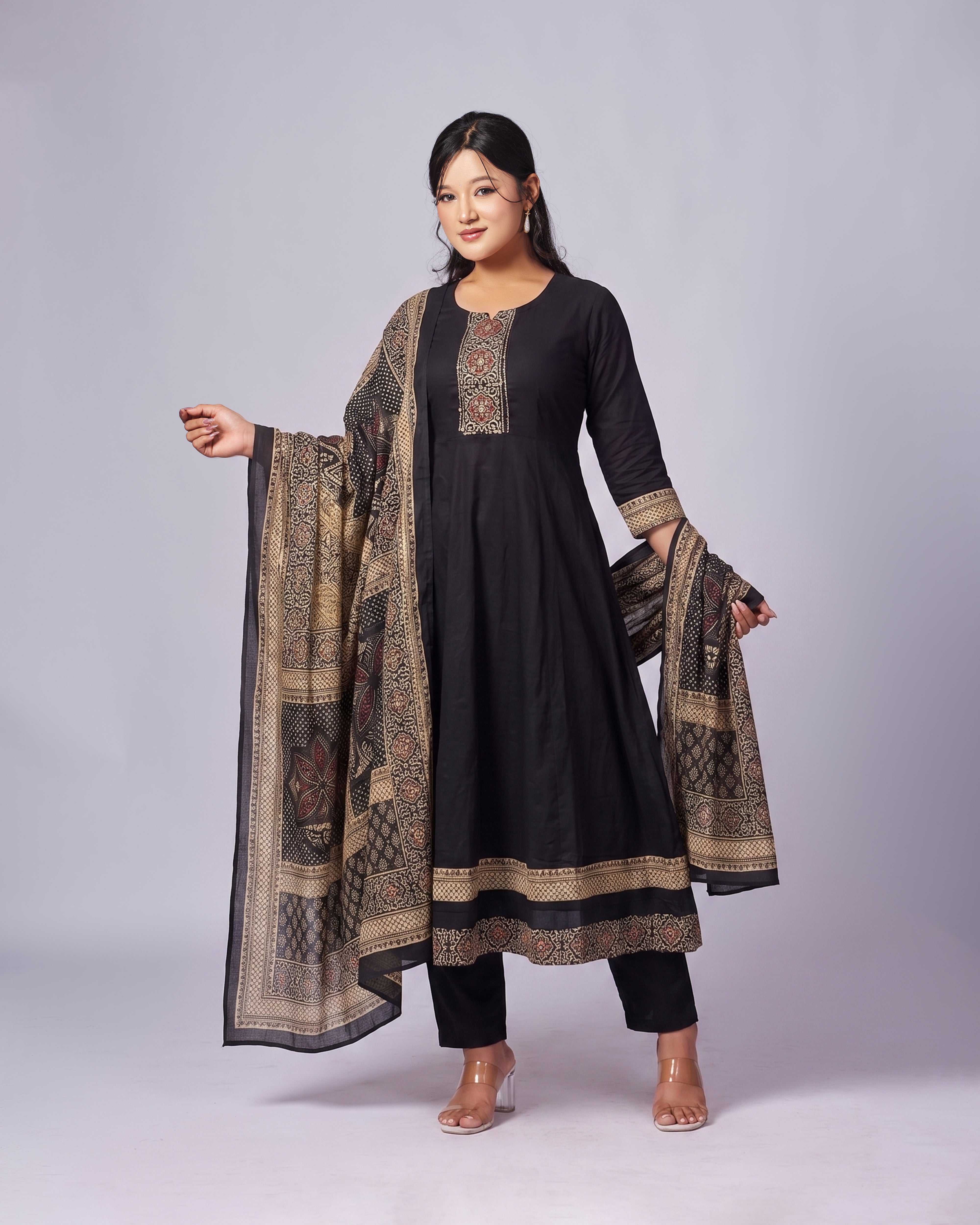 Woman wearing a black traditional outfit with a patterned dupatta on a gray background