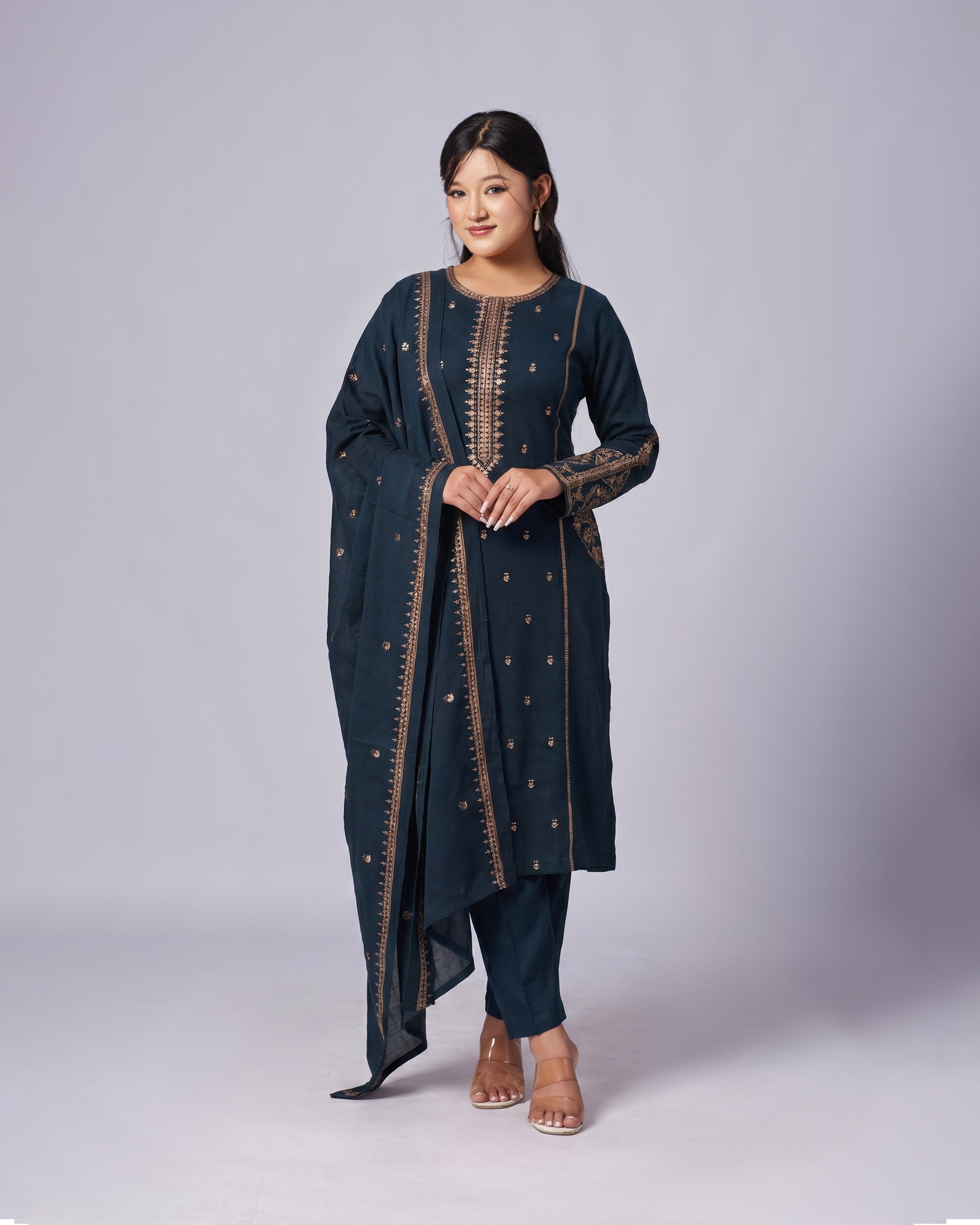 Woman wearing a dark blue traditional outfit with intricate patterns on a light gray background