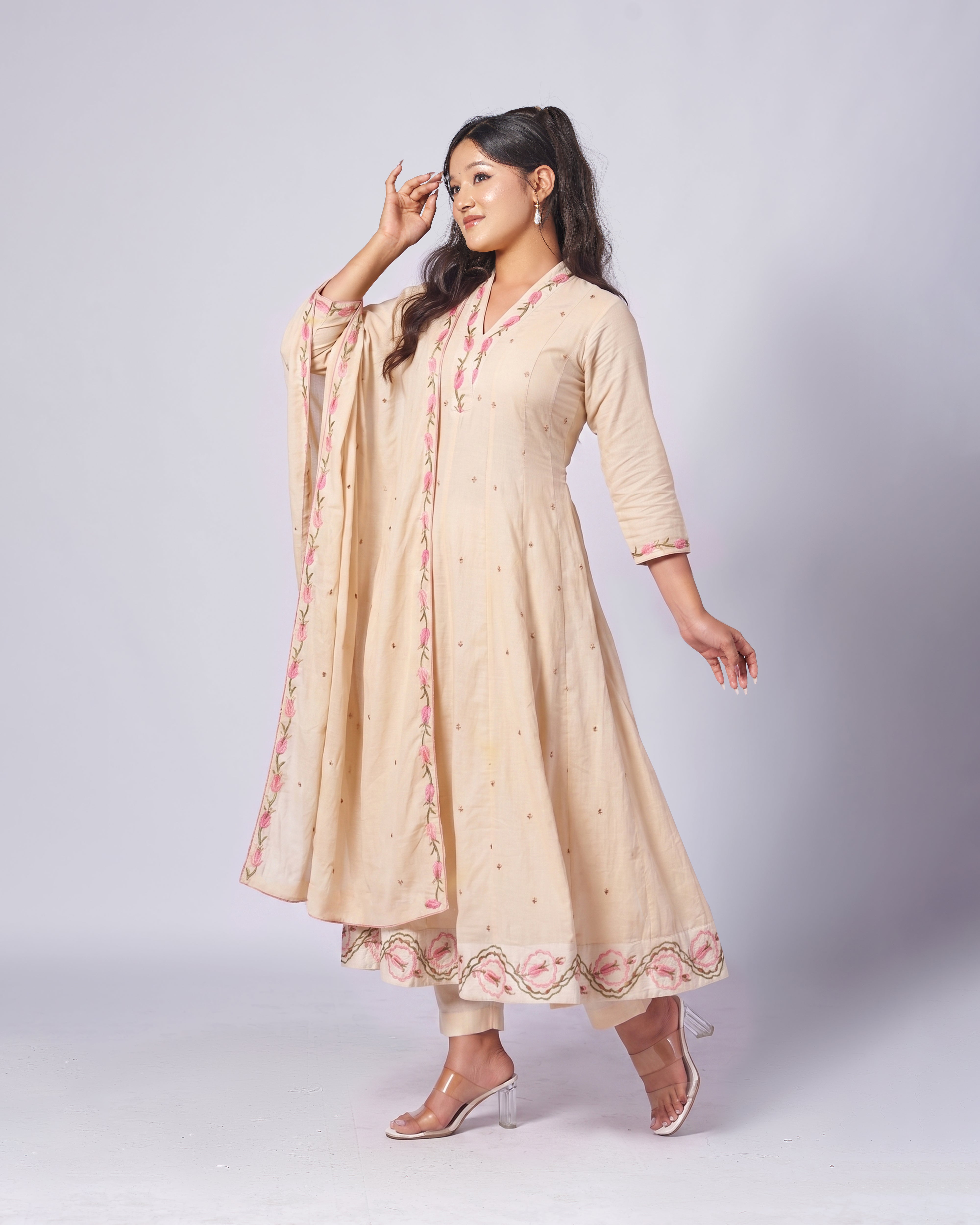 Woman wearing a beige traditional outfit with floral embroidery on a white background
