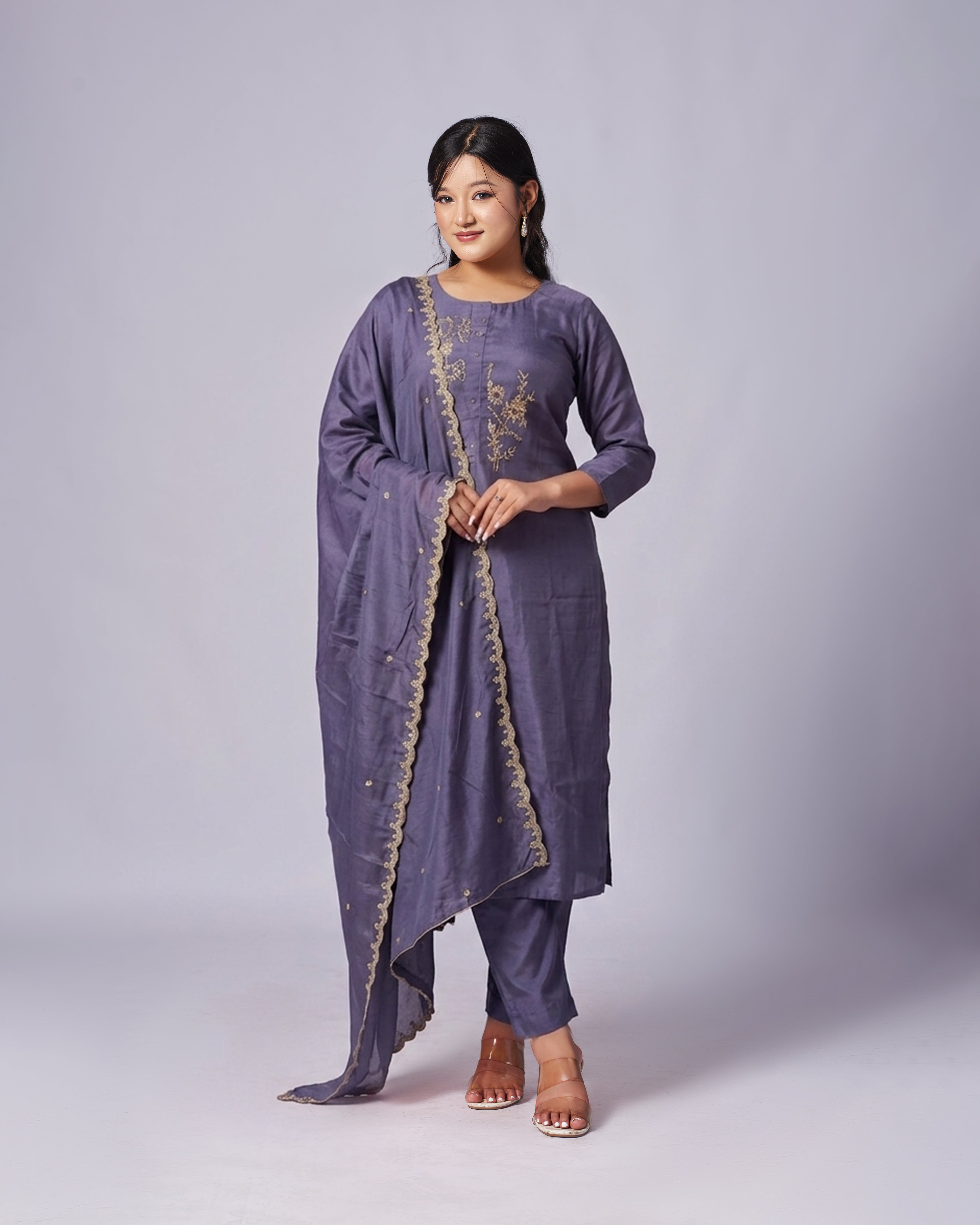 Woman wearing a purple traditional outfit with gold embroidery on a gray background