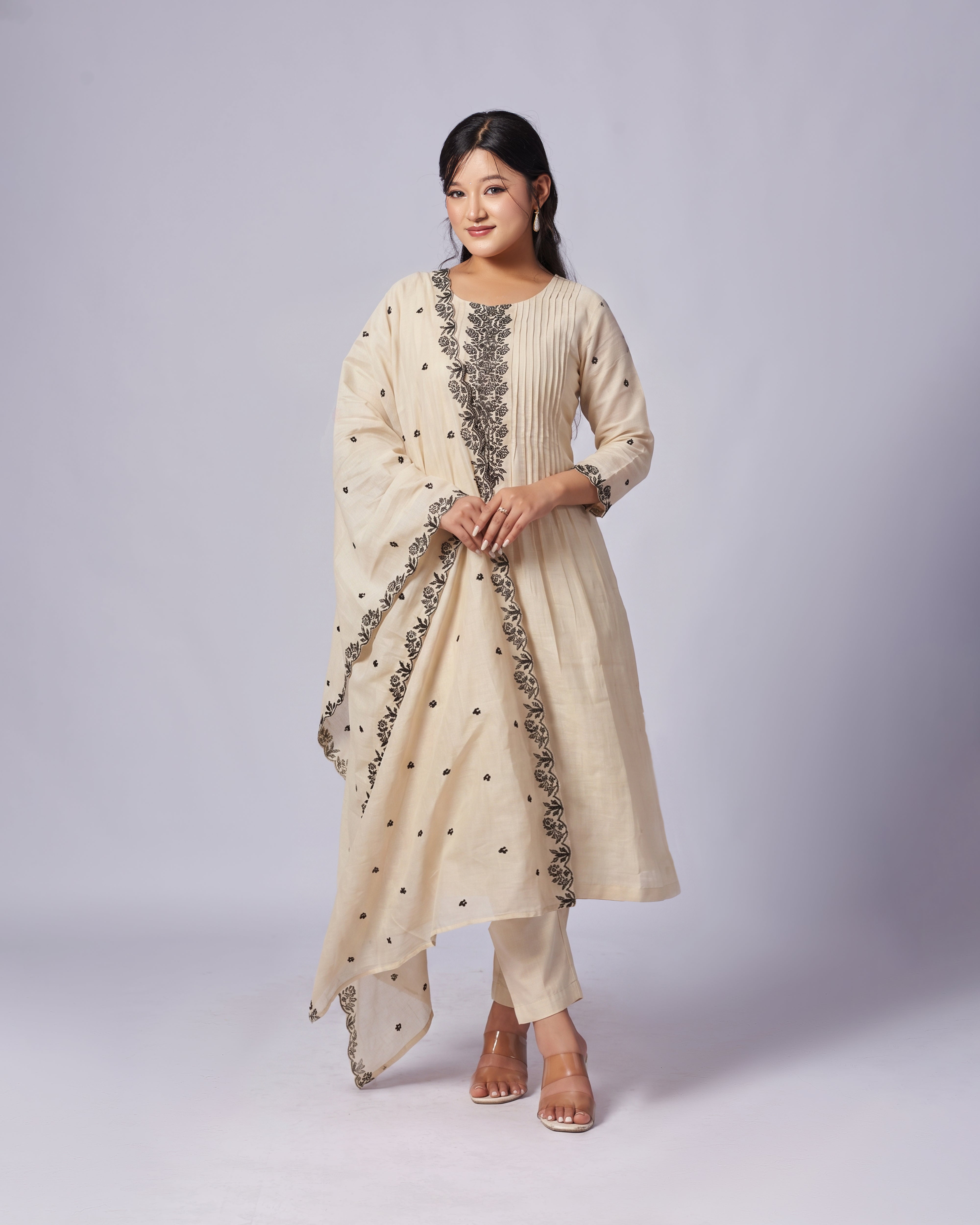 Woman wearing a cream-colored traditional outfit with black embroidery on a white background