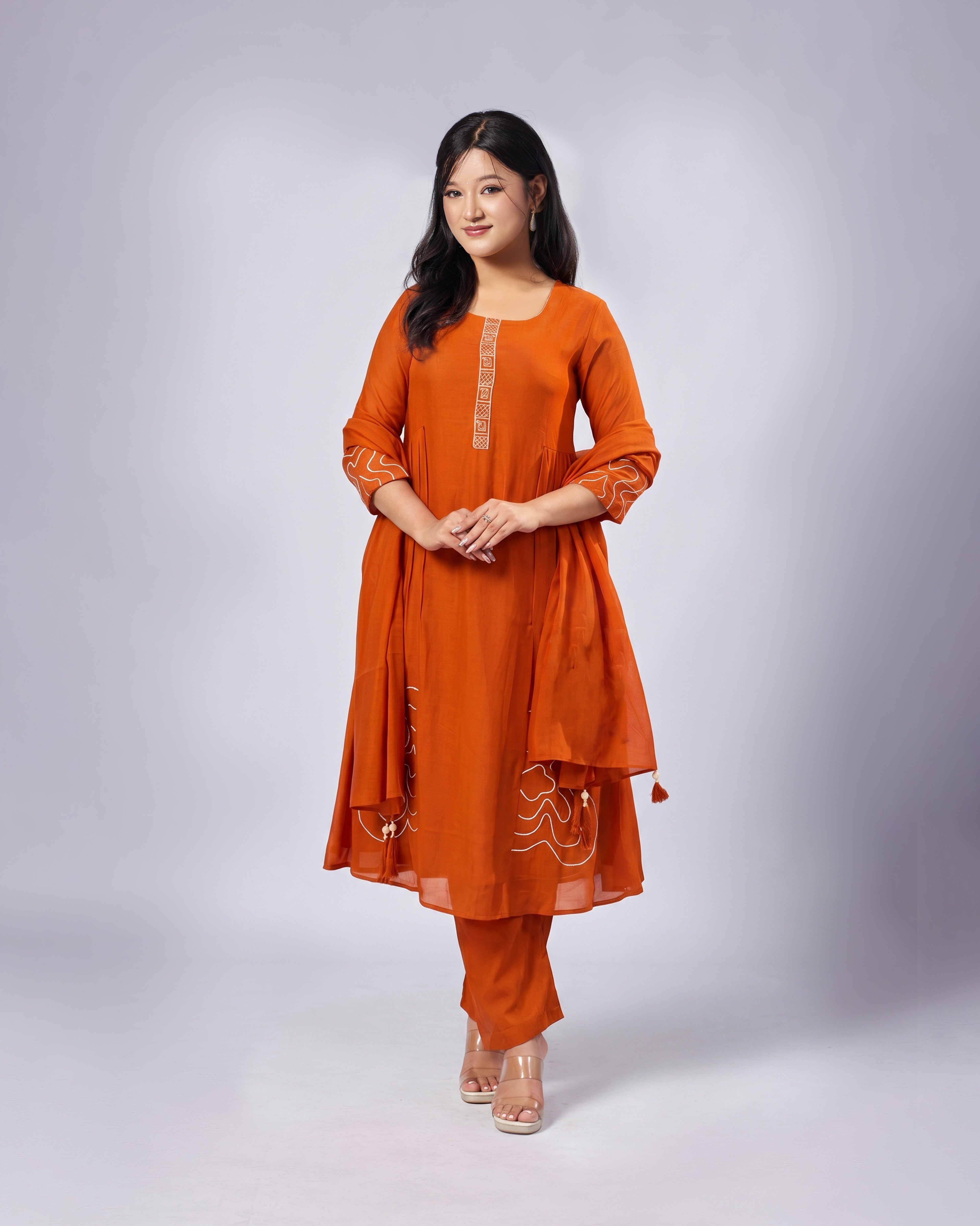 Woman wearing an orange traditional outfit with white patterns on a light gray background