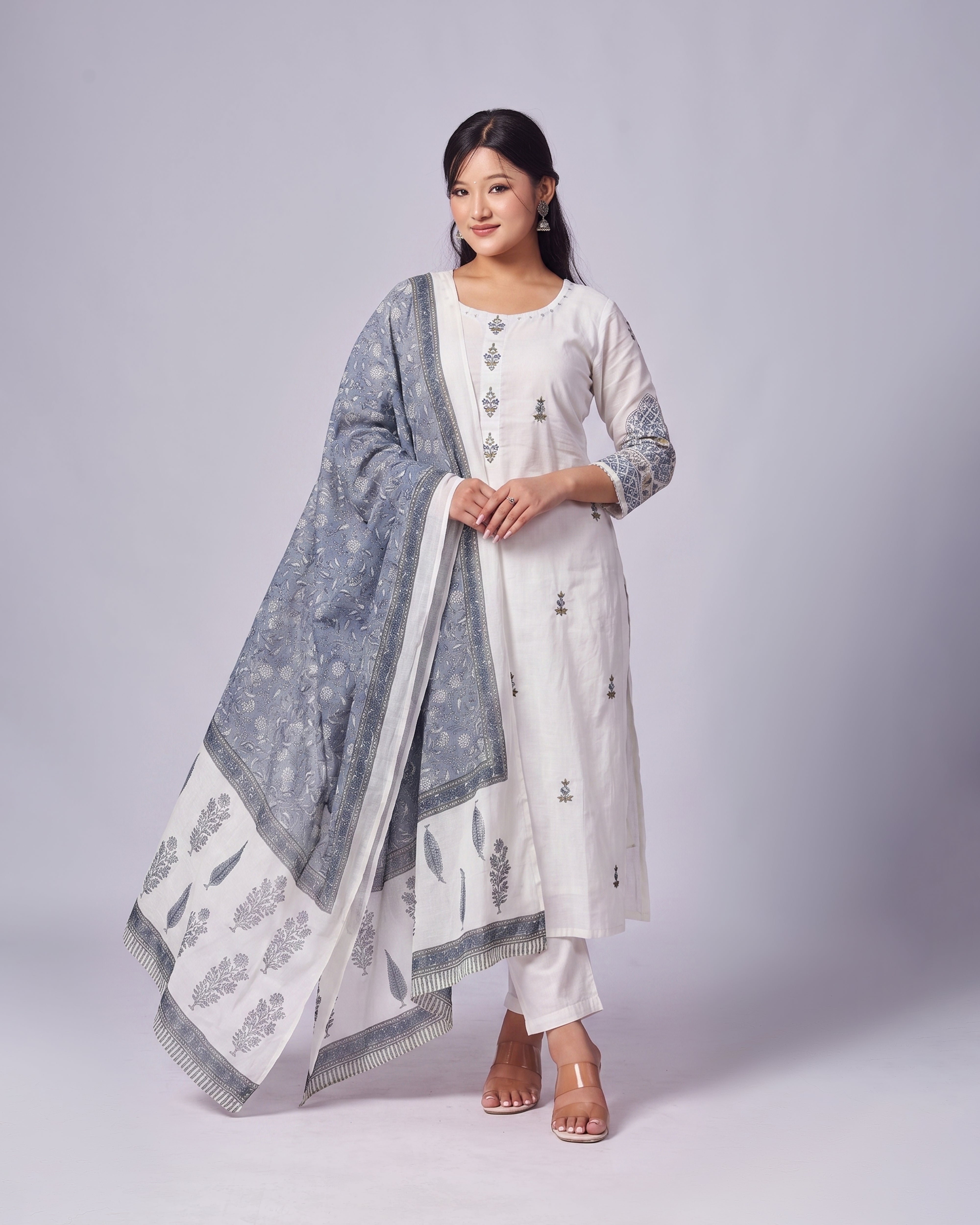 Woman wearing a white kurta with blue patterns and a matching dupatta on a gray background