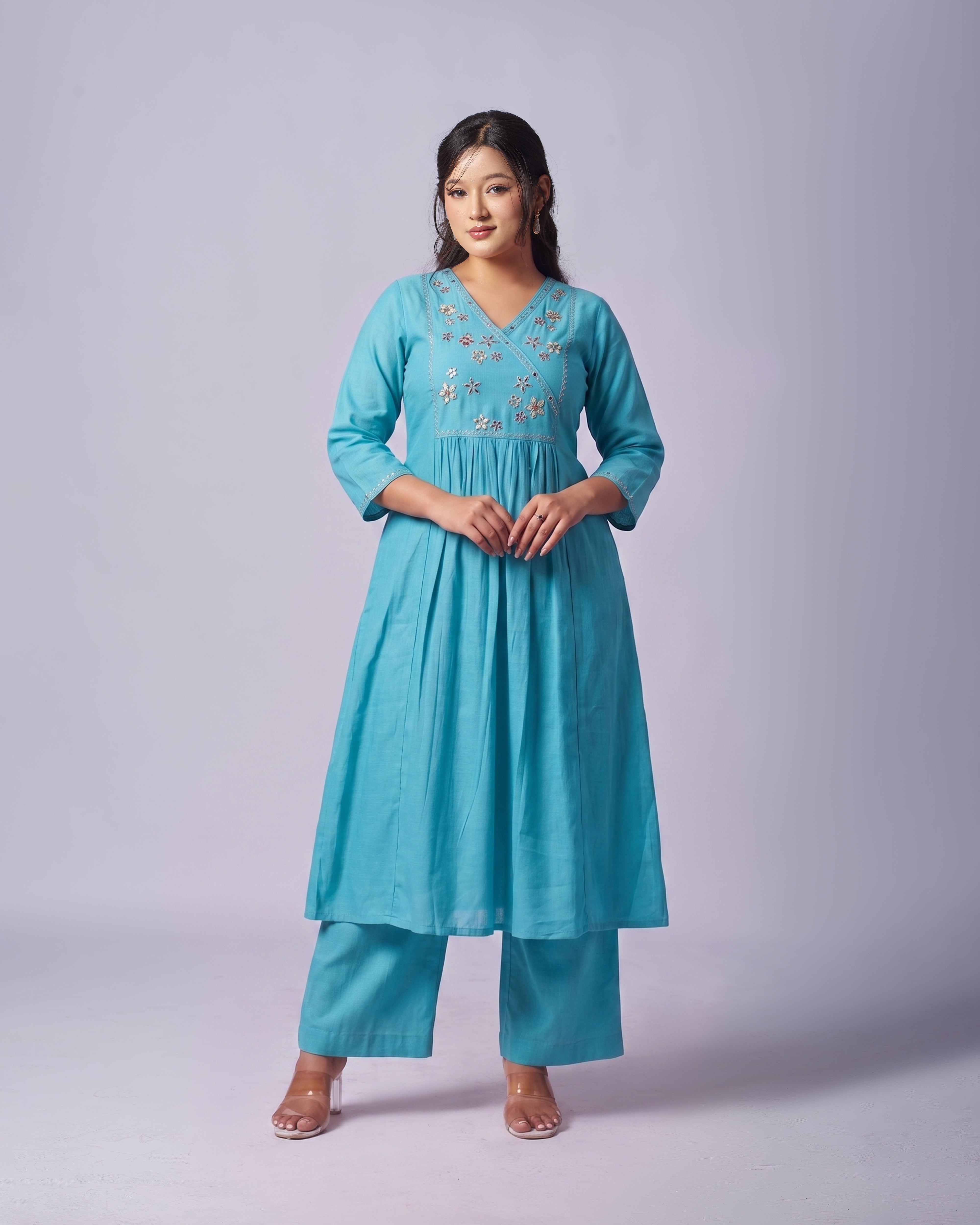 Woman wearing a turquoise embroidered outfit on a plain background