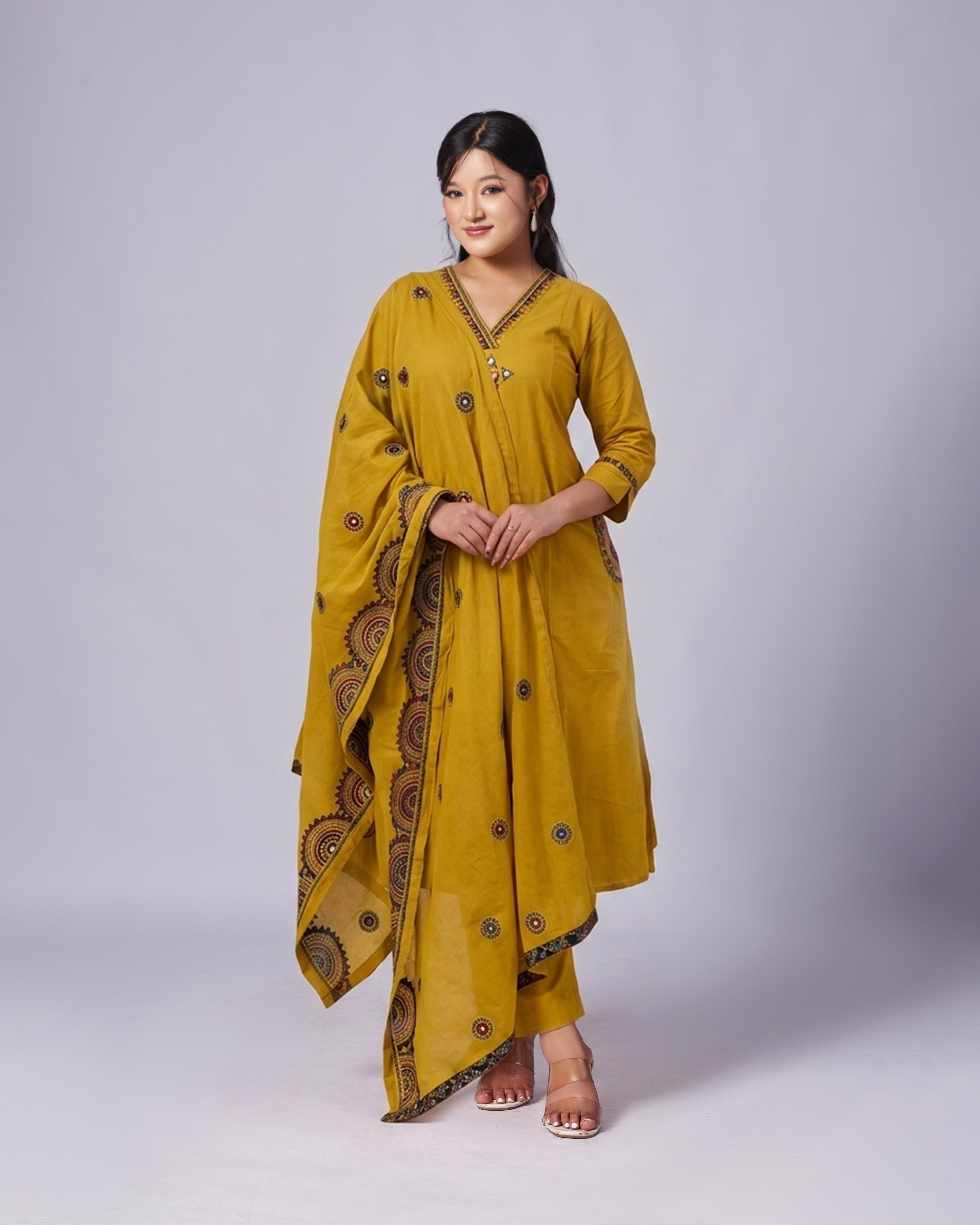 Woman wearing a mustard yellow traditional outfit with a patterned dupatta on a white background