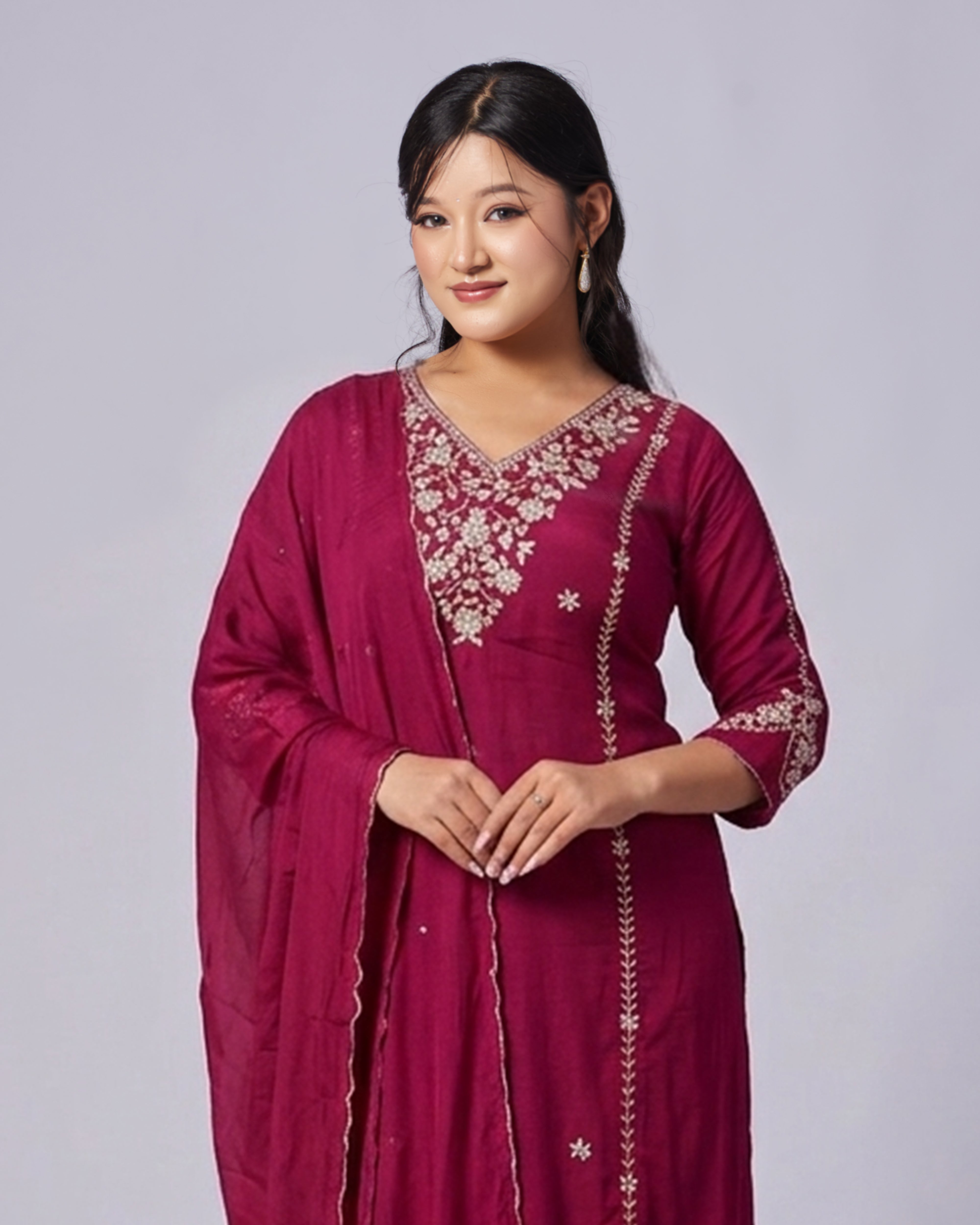 Woman wearing a maroon traditional outfit with intricate embroidery on a plain background