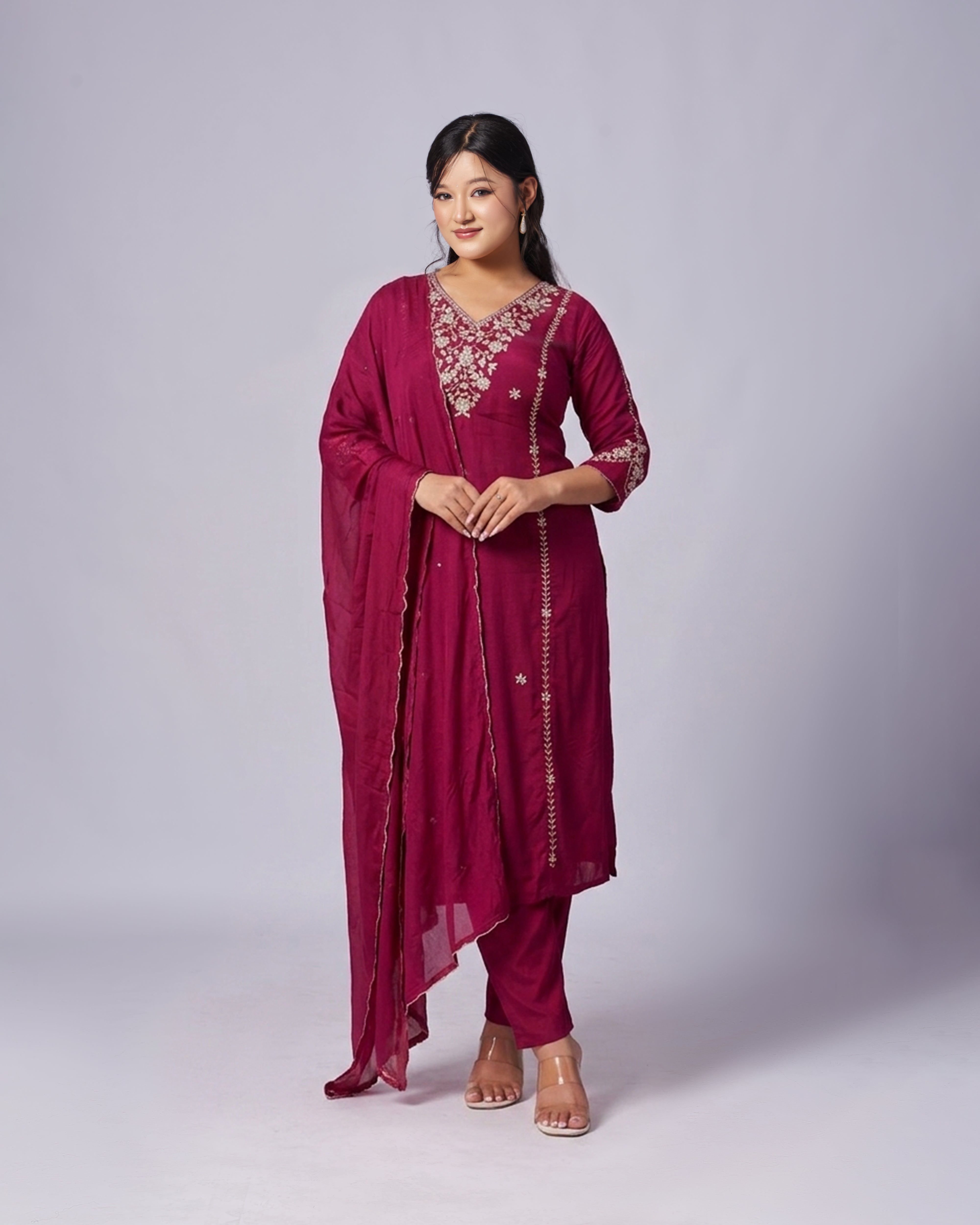 Woman wearing a maroon traditional outfit with gold embroidery on a white background
