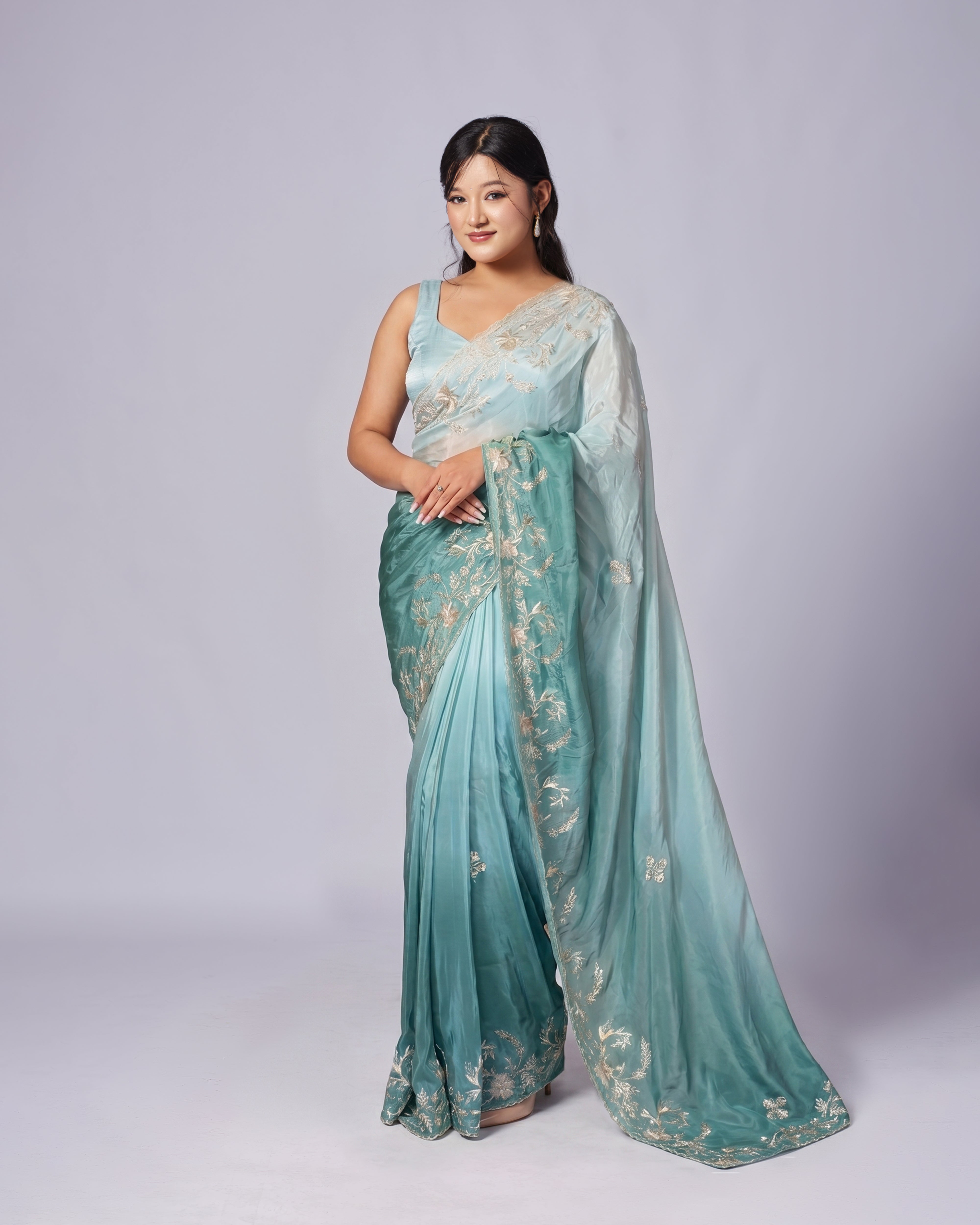 Woman wearing a light blue saree with gold patterns on a white background