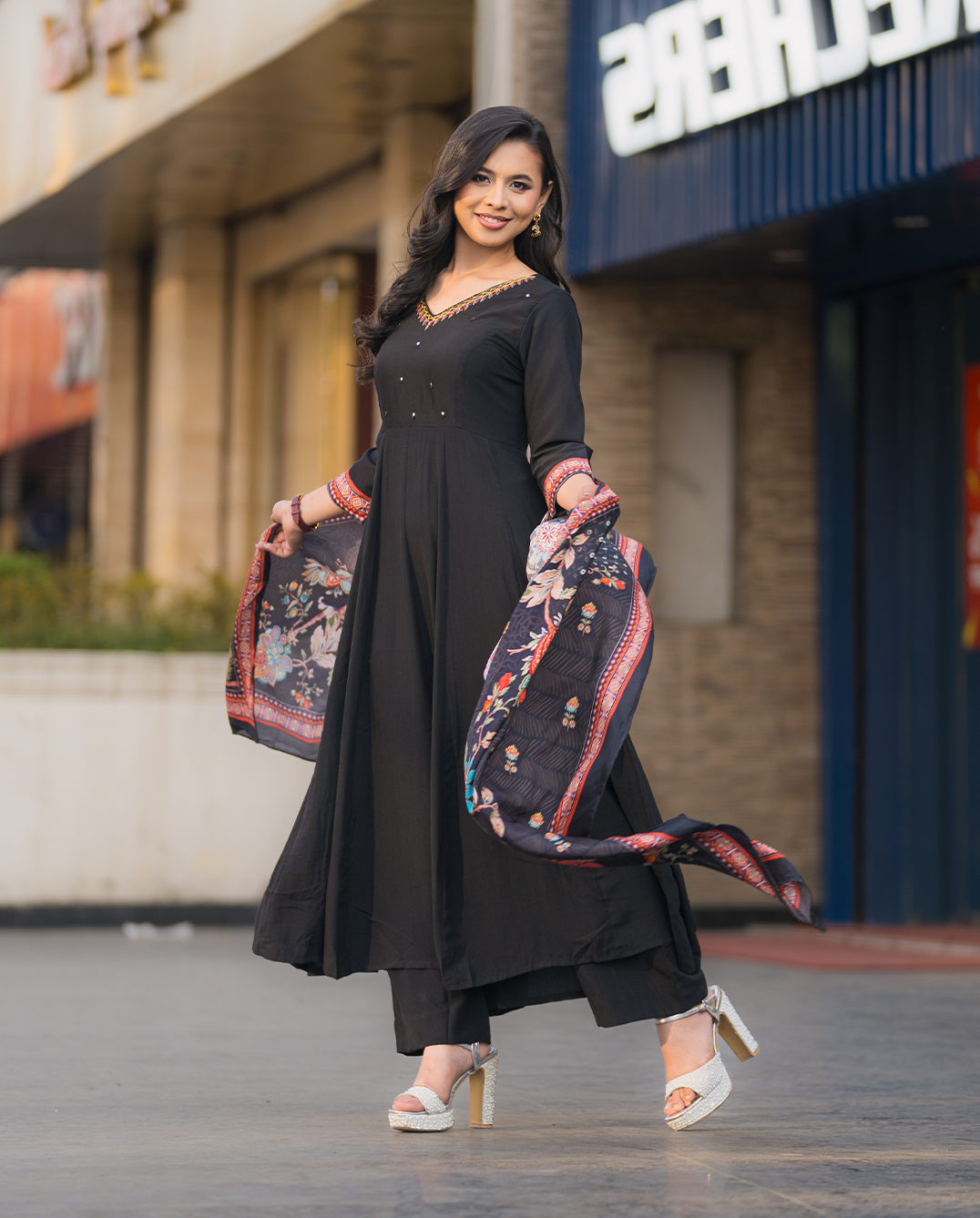 Woman in a black outfit with a patterned scarf standing on a street.