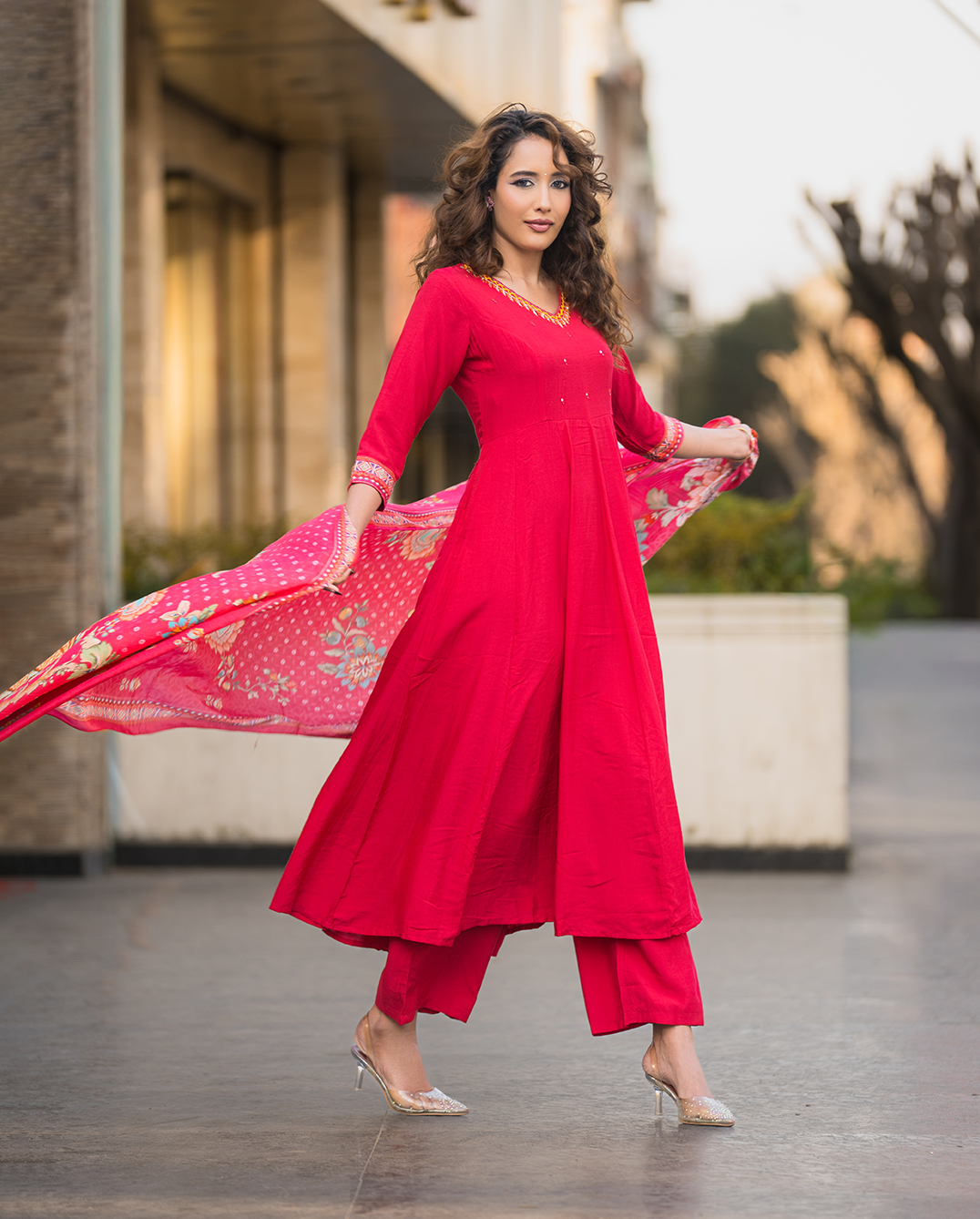 Woman in a red traditional outfit with a pink dupatta, standing outdoors.