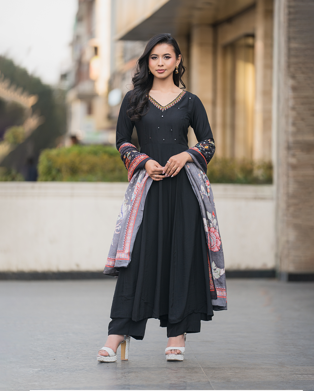 Woman in a black traditional outfit with a patterned shawl standing outdoors.