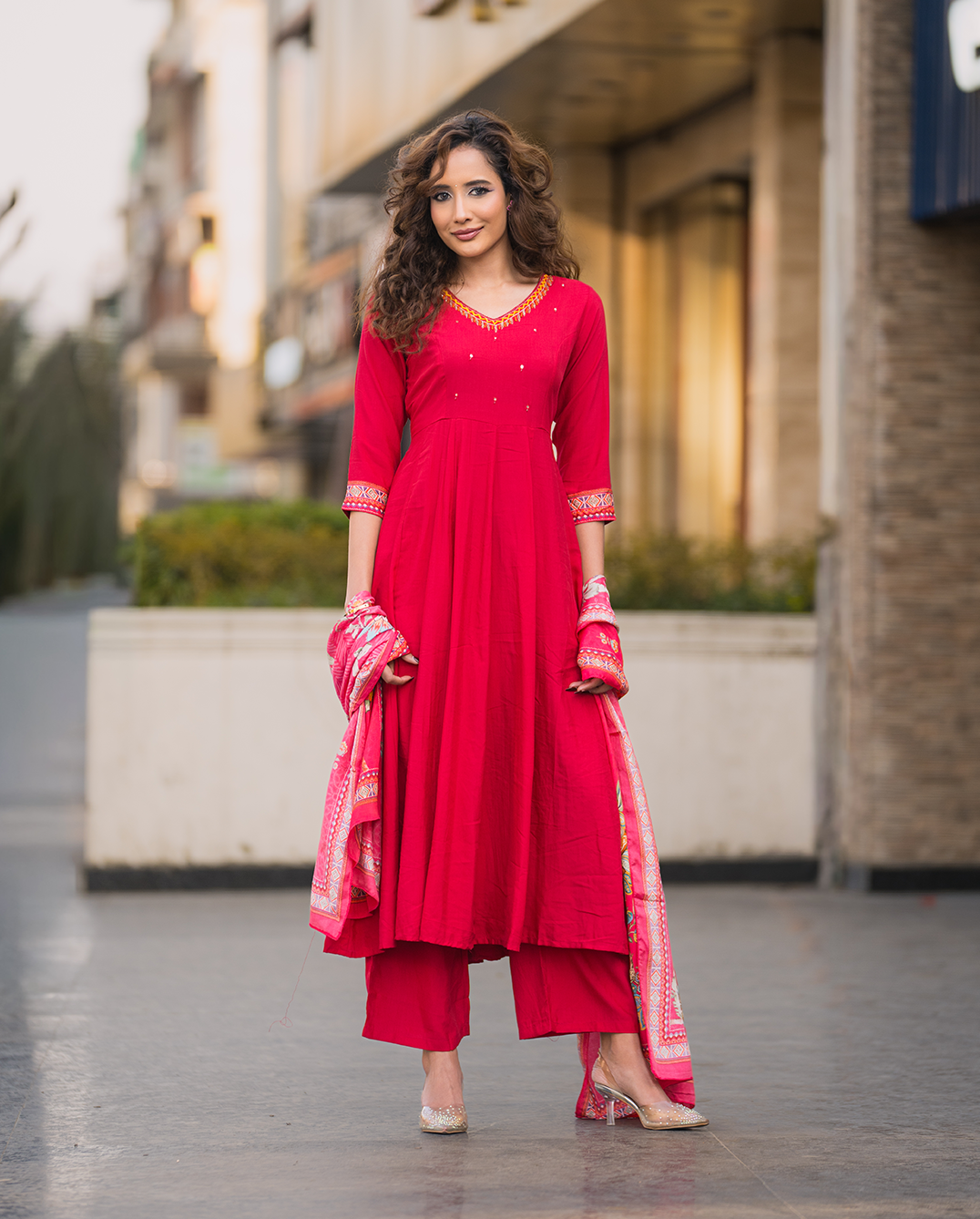 Woman in a red traditional outfit standing on a street.