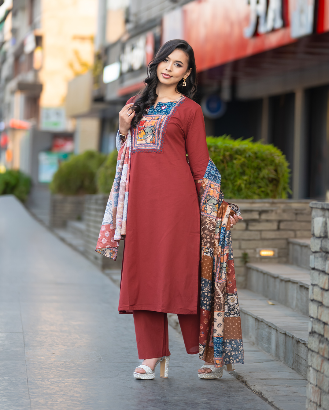 Woman in a red traditional outfit with floral patterns walking on a street.