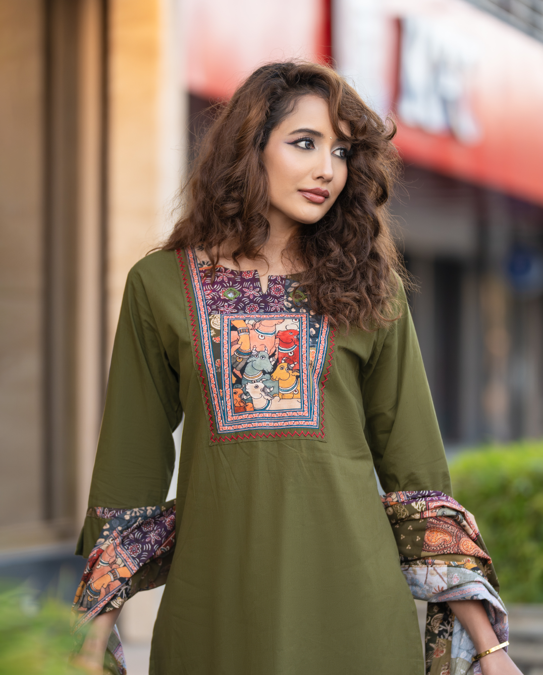 Woman wearing a green embroidered dress with colorful patterns in an urban setting