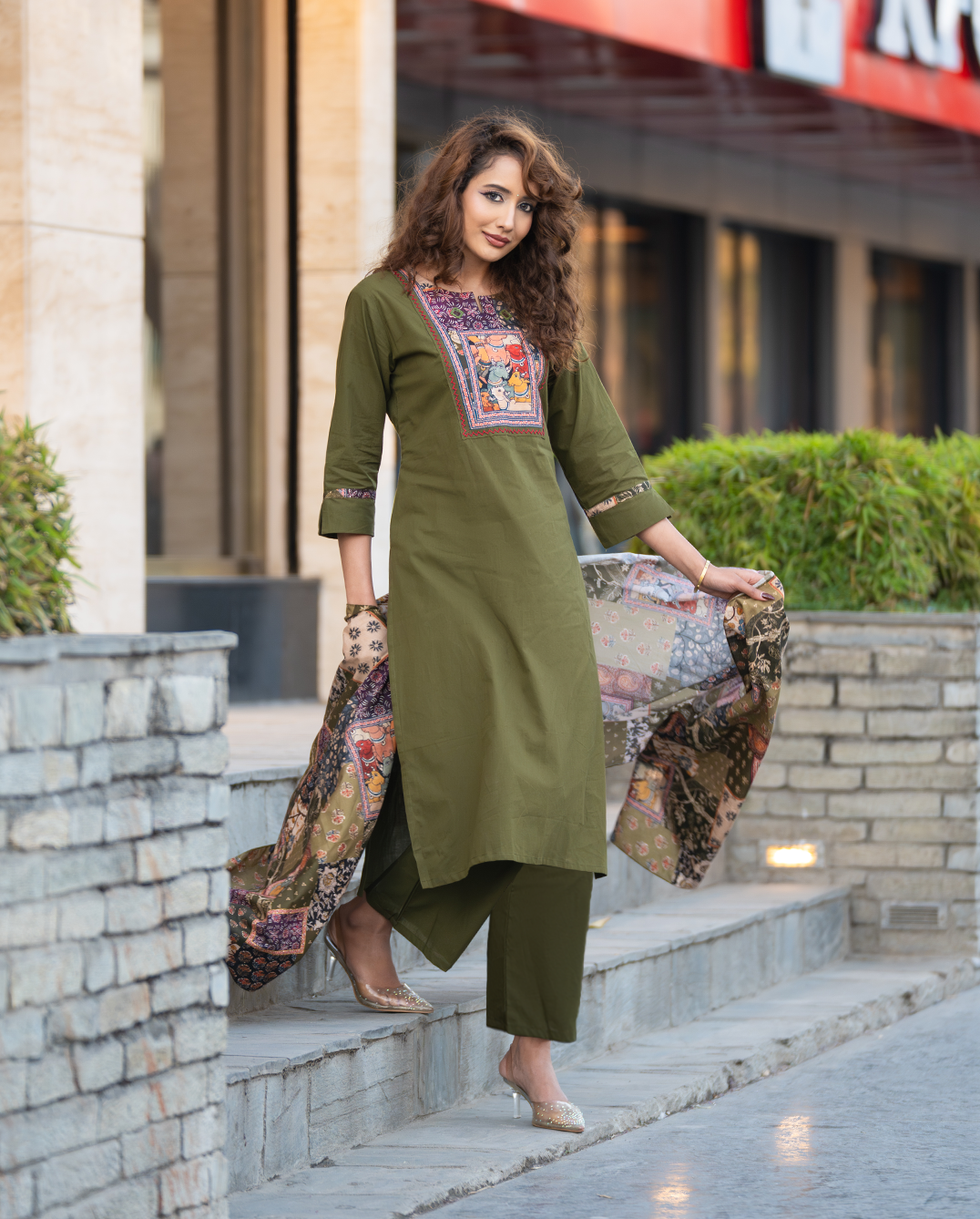 Woman in green traditional outfit with floral dupatta standing outdoors.