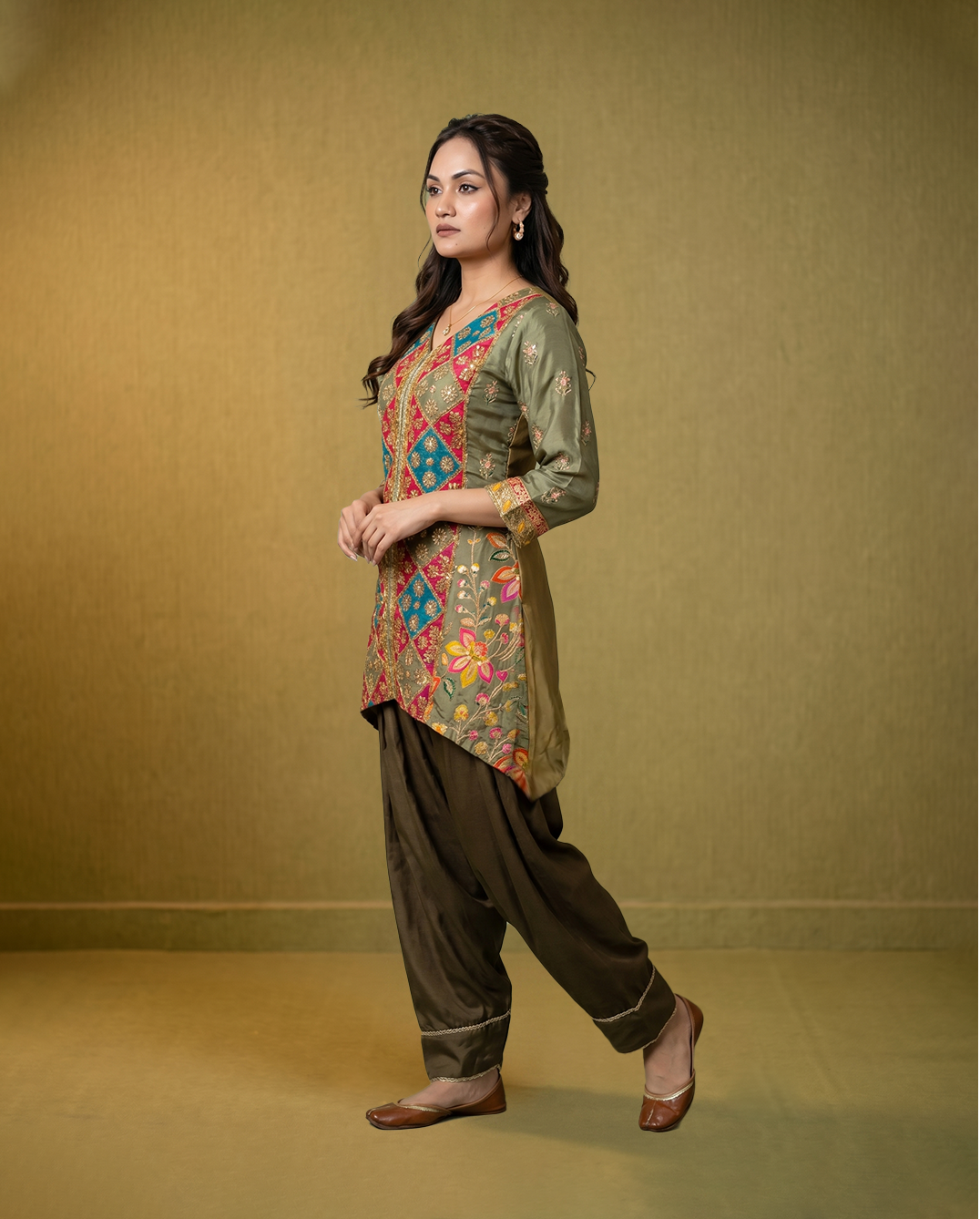 Woman wearing a traditional outfit with a colorful top and dark pants on a gold background