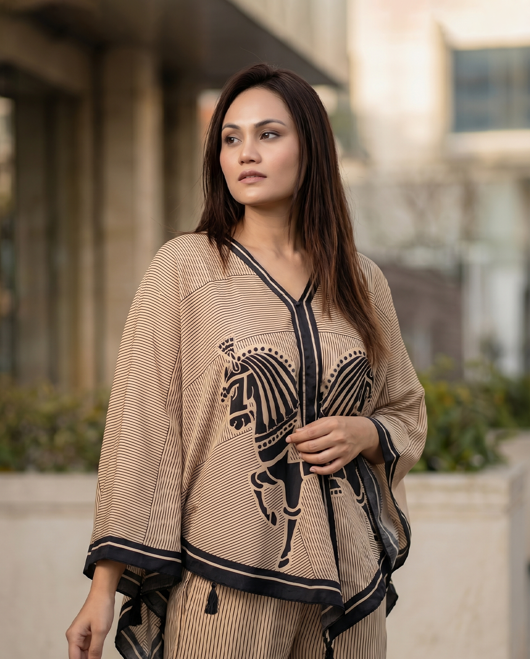 Woman wearing a beige and black patterned outfit with a horse design outdoors.