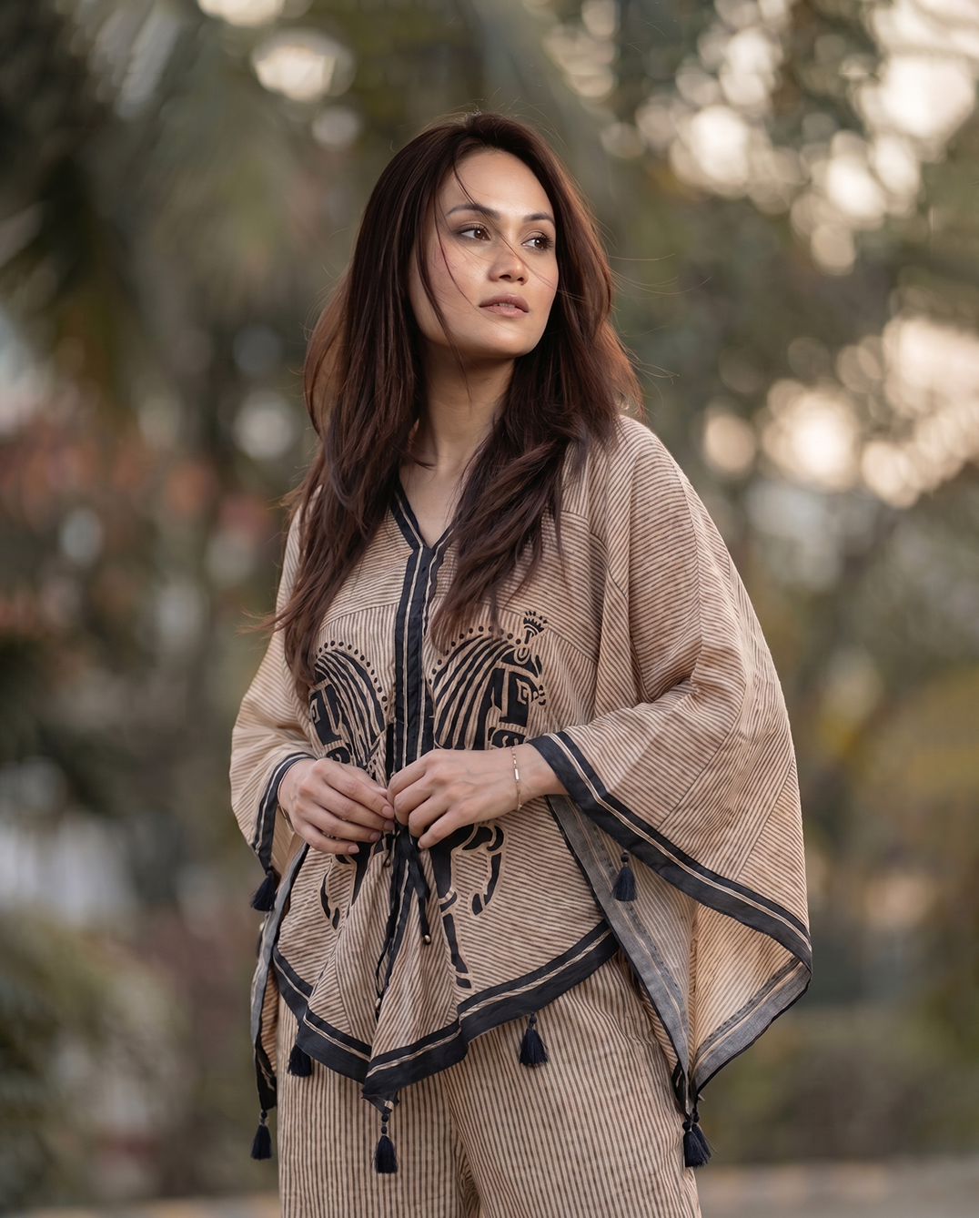 Woman wearing a beige embroidered outfit with tassels in a natural setting
