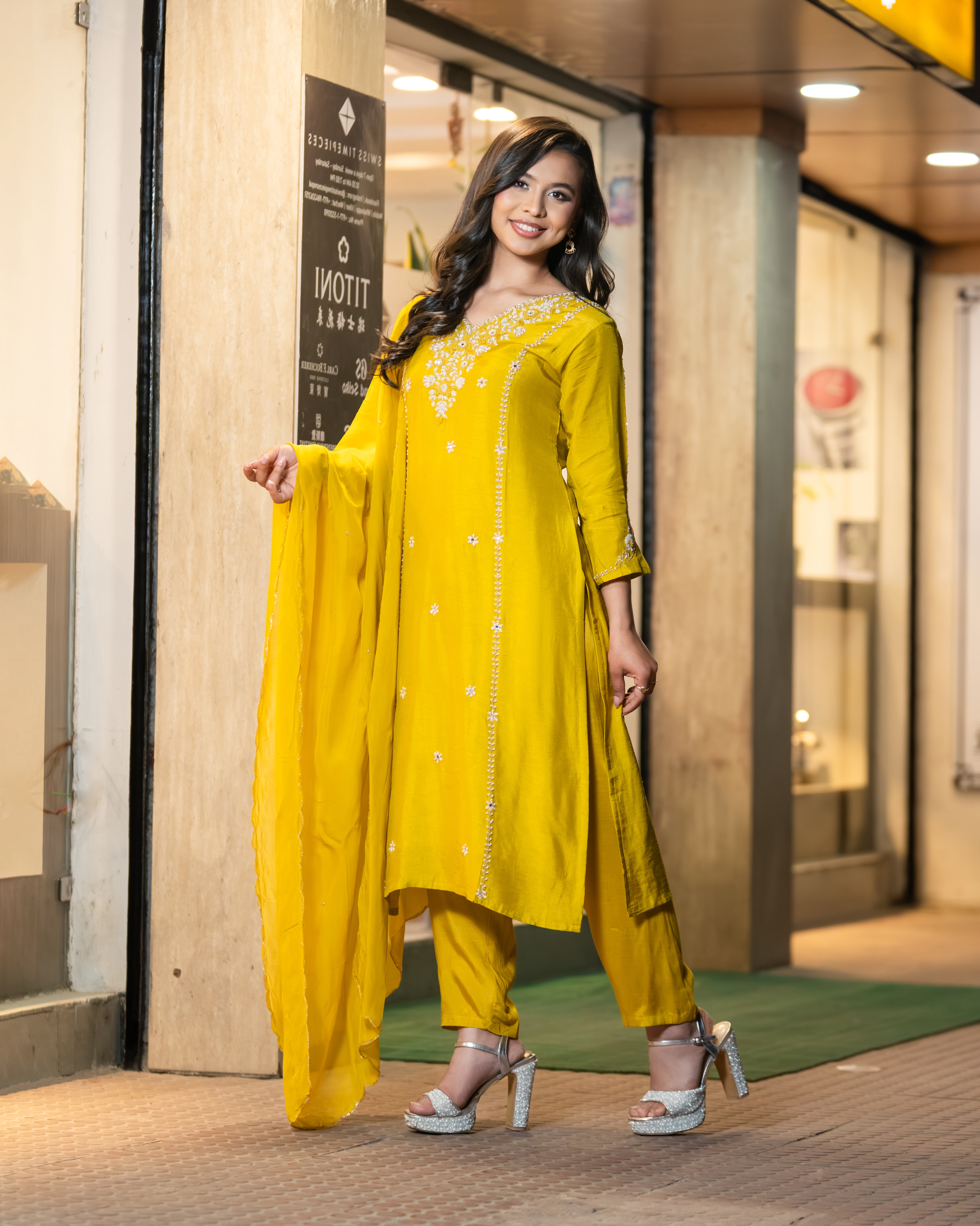Woman in a yellow traditional outfit standing in front of a store entrance.