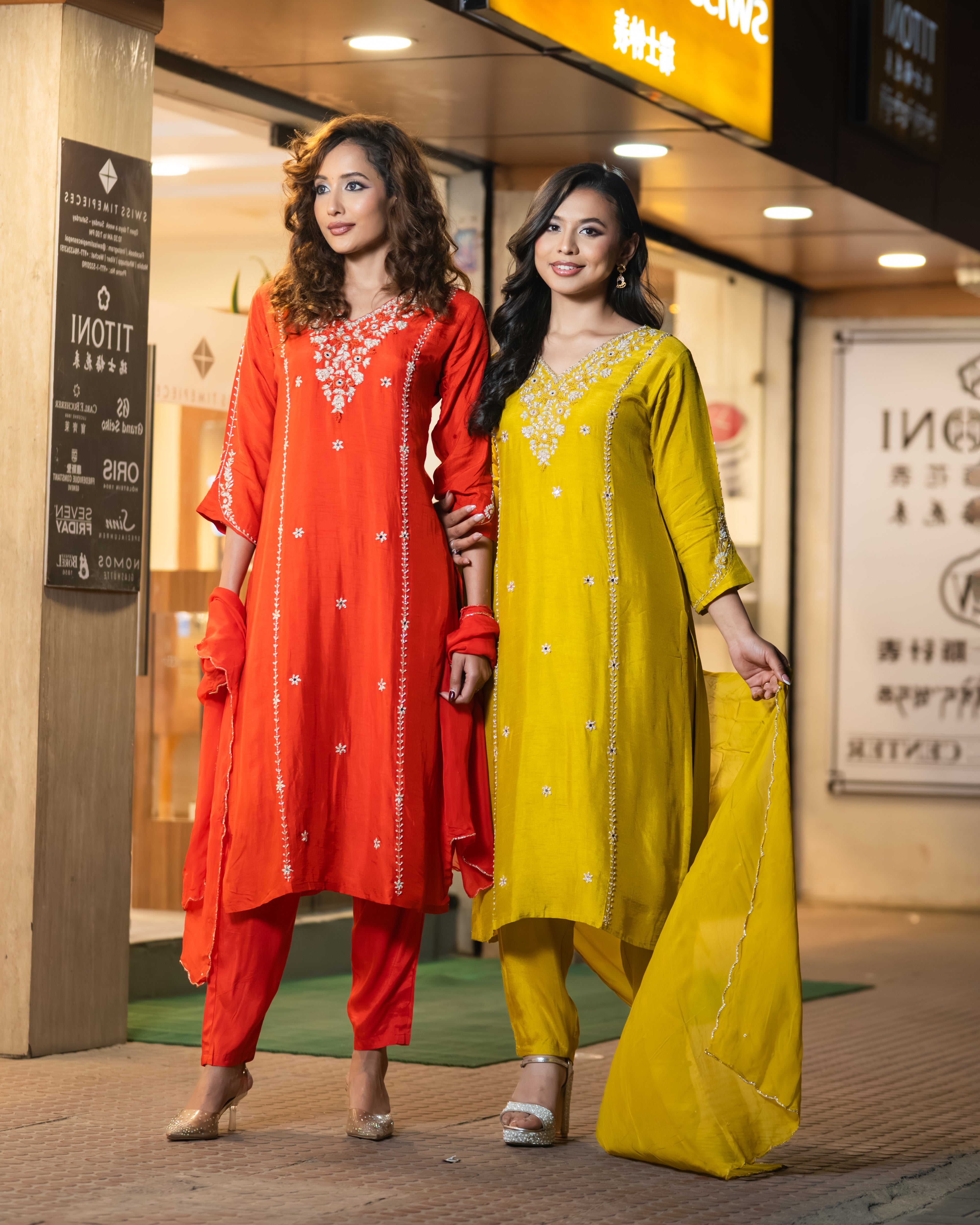 Two women in red and yellow traditional outfits standing in a shopping mall.