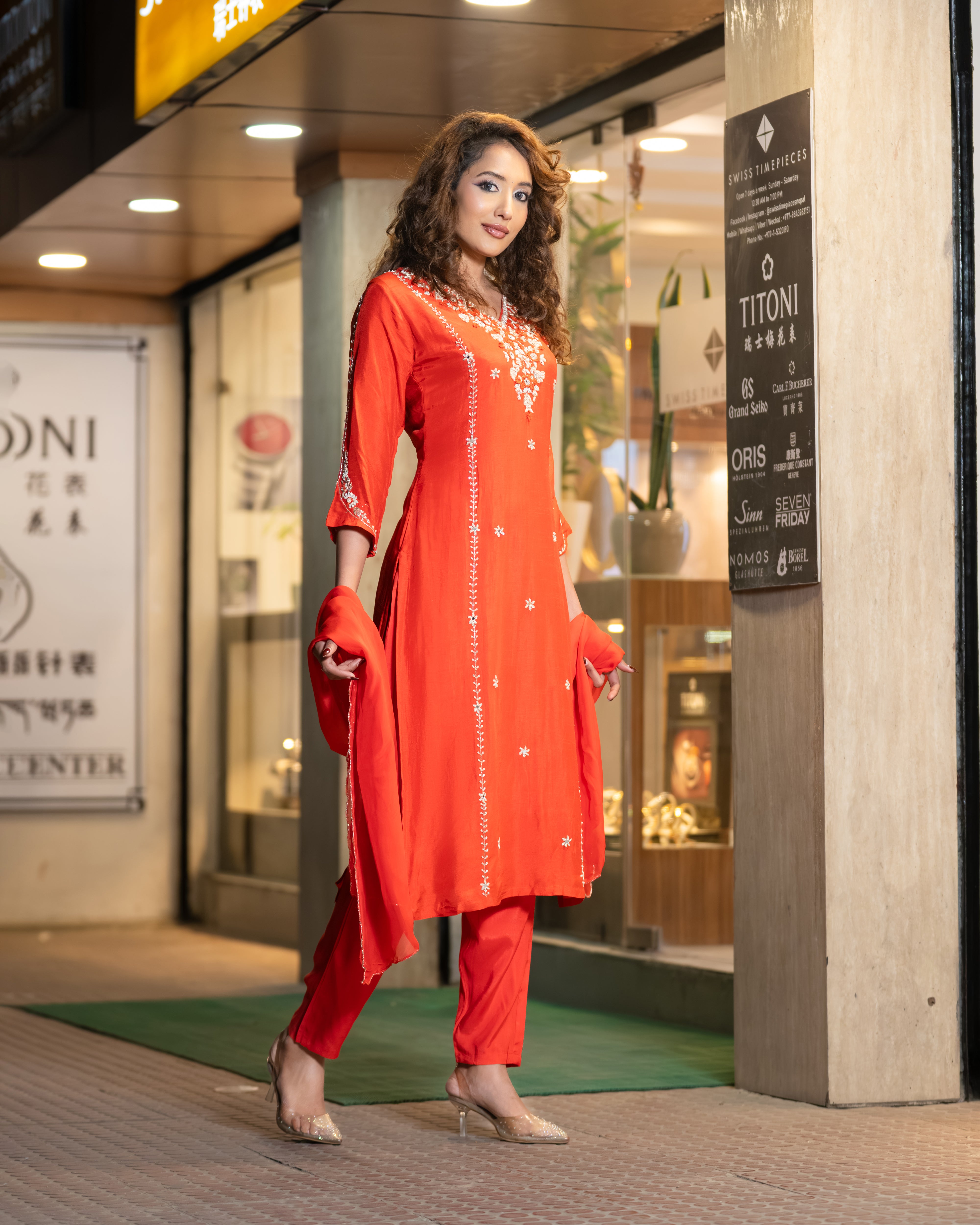 Woman in an orange traditional outfit standing in front of a store entrance.