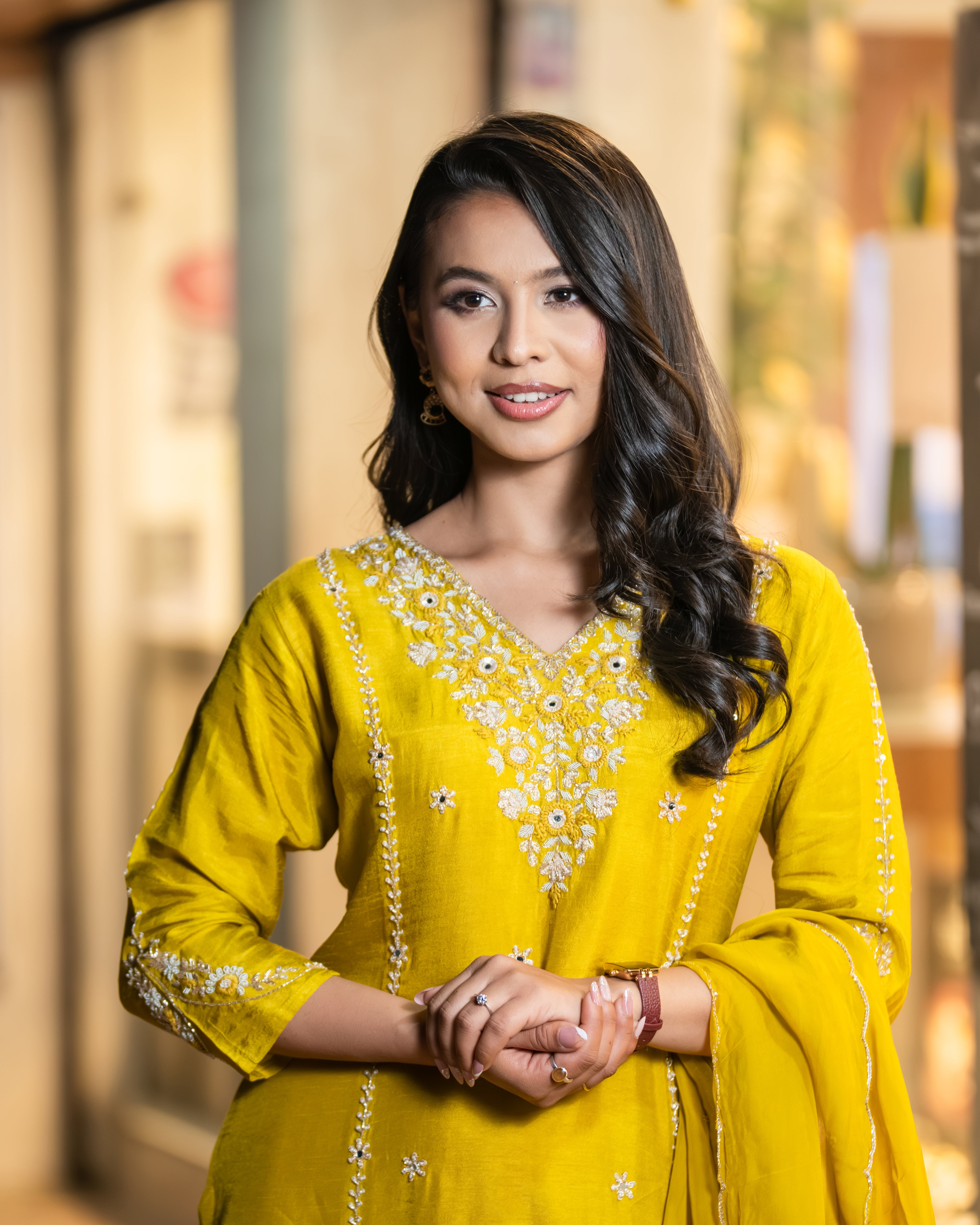 Woman wearing a yellow traditional outfit with floral patterns indoors.