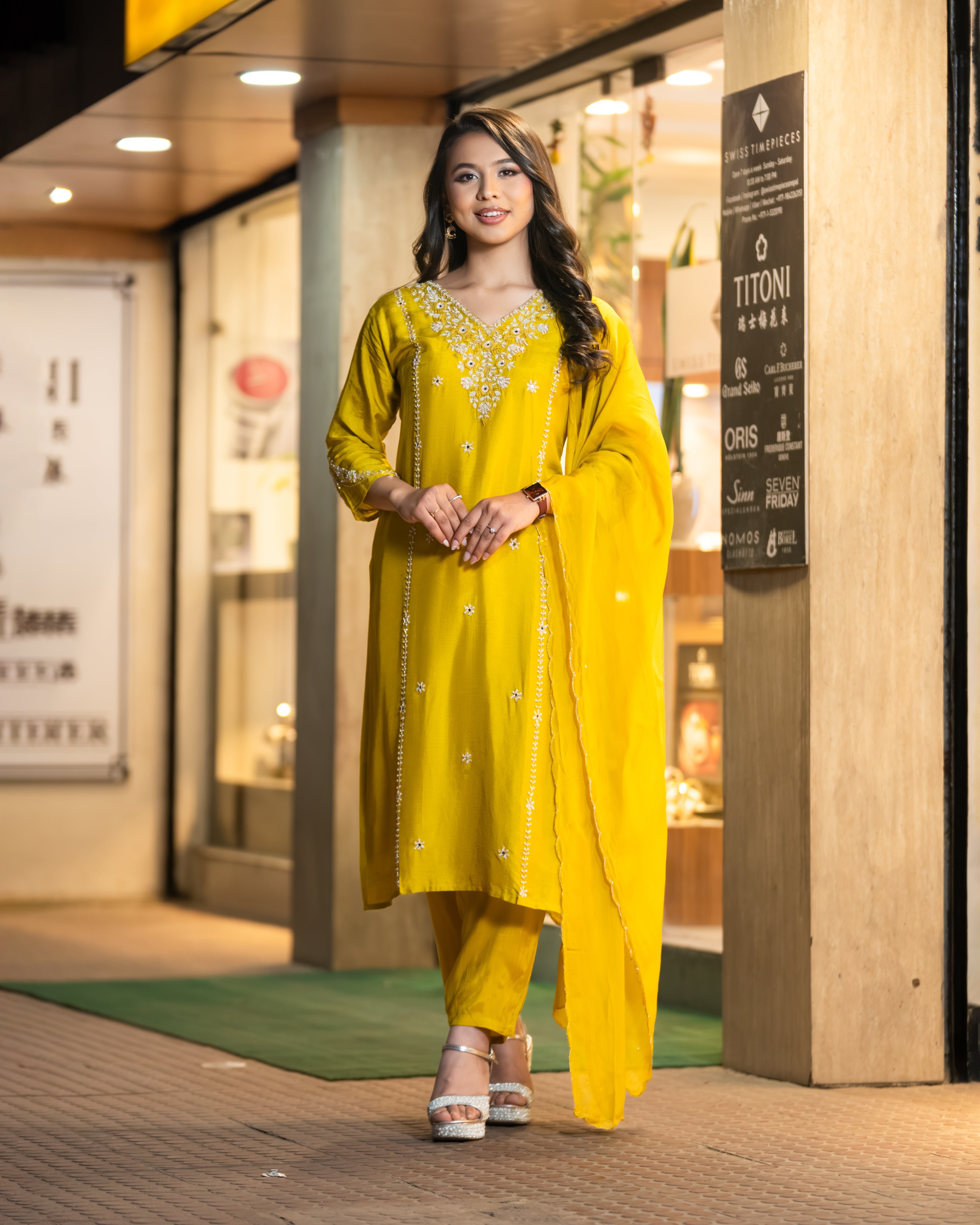 Woman in a yellow traditional outfit standing in front of a store entrance.