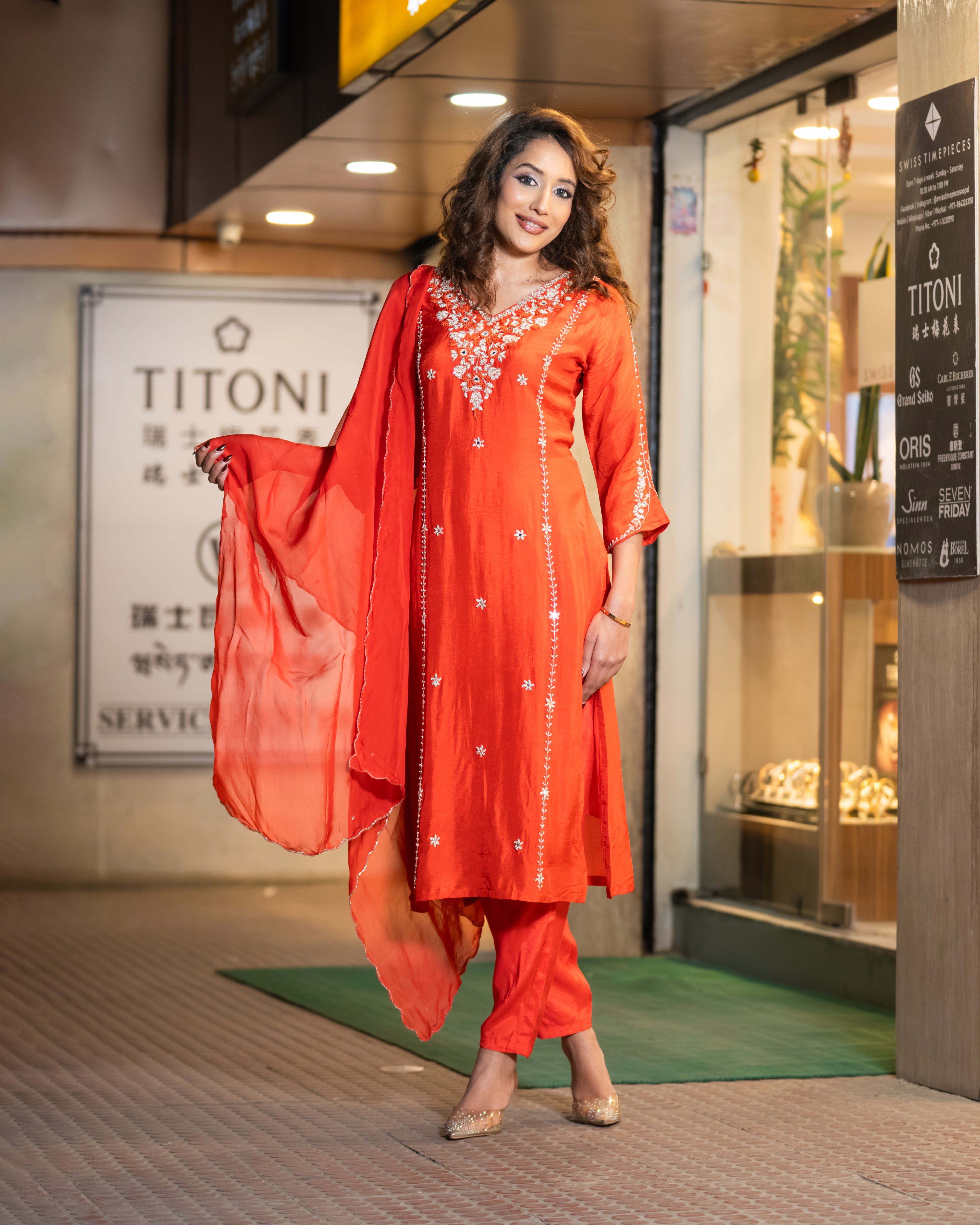 Woman in an orange traditional outfit standing in front of a store entrance.