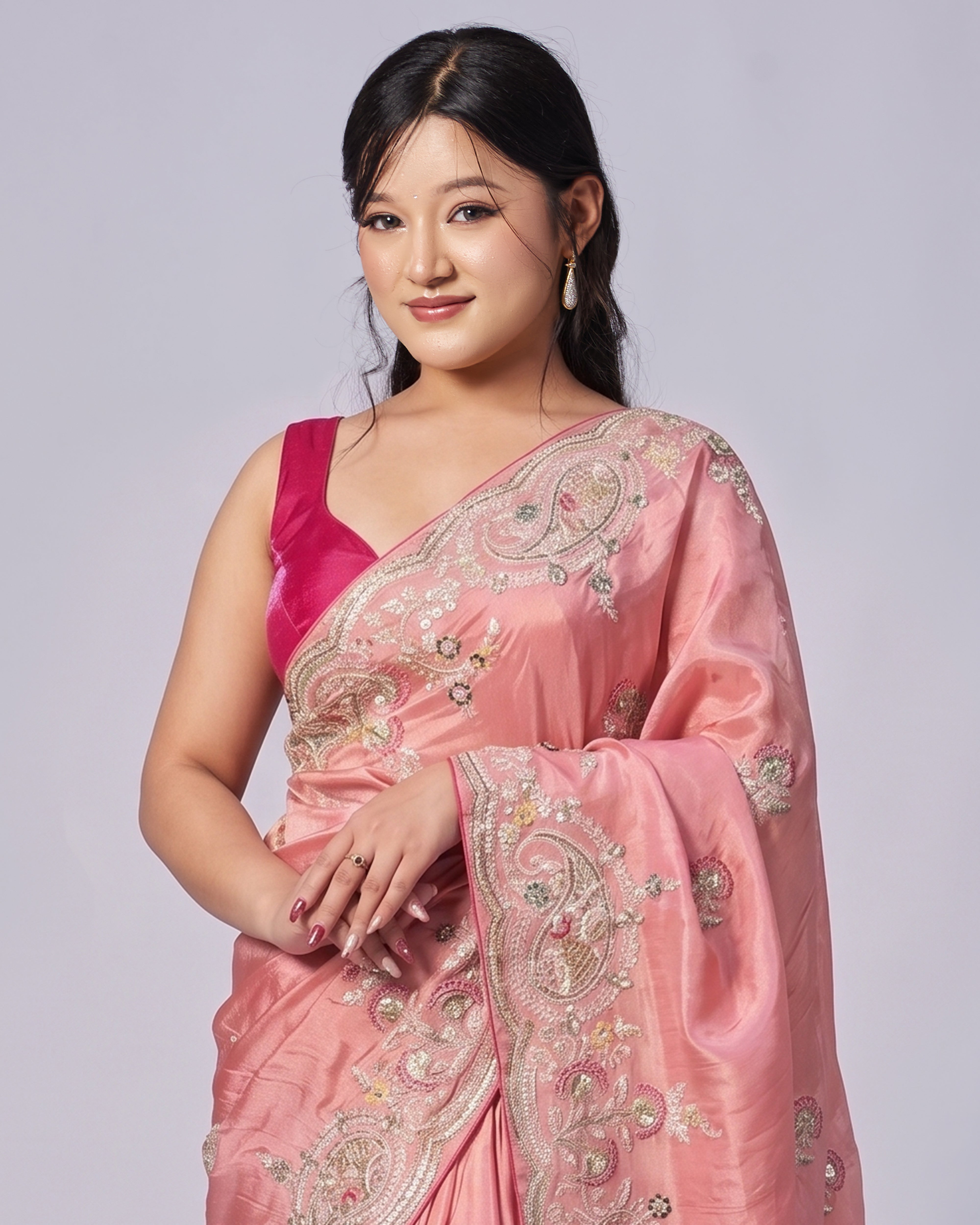 Woman wearing a pink saree with intricate designs on a plain background