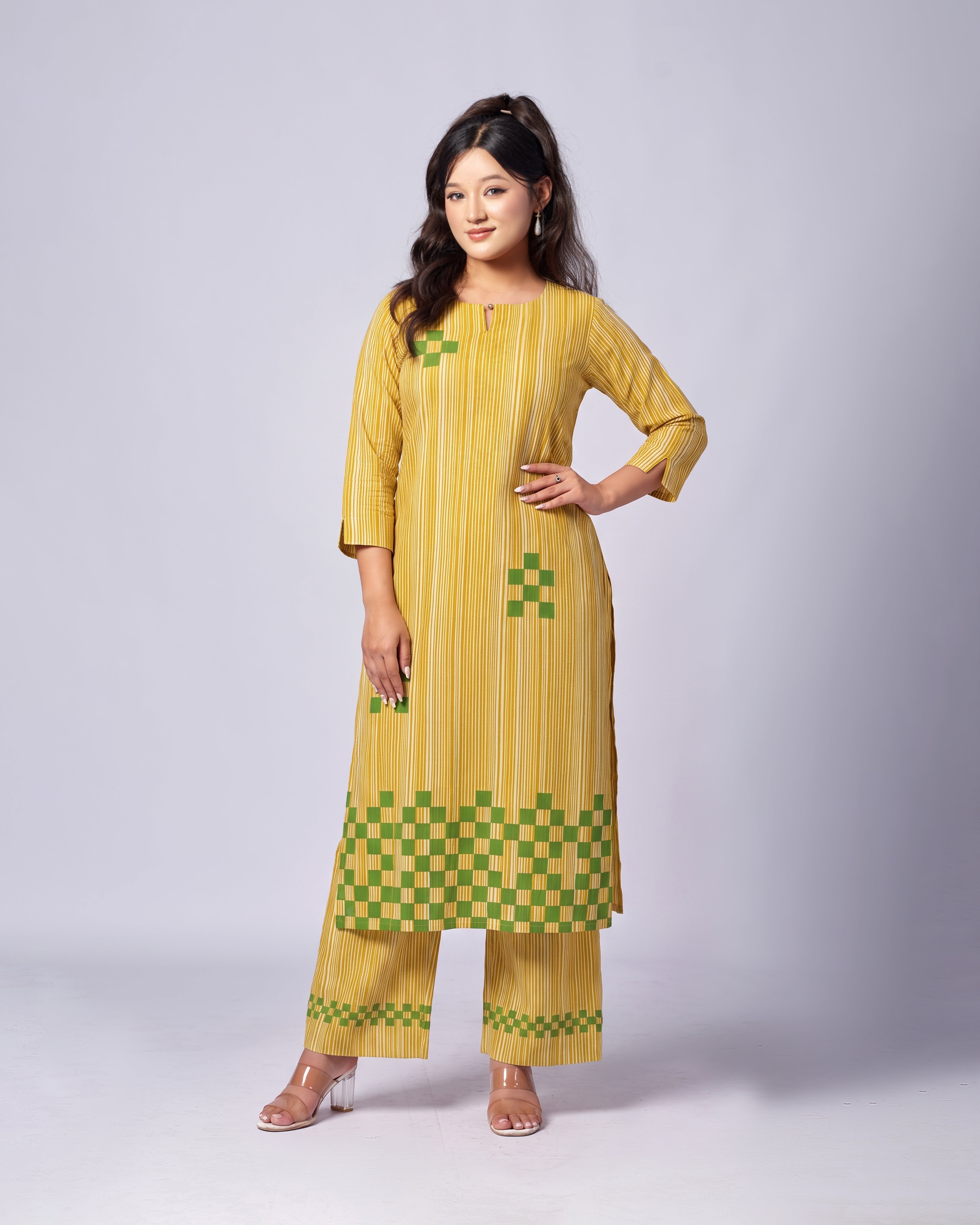 A woman modeling a yellow and green checkered kurta set with matching wide-leg pants against a light gray studio background.