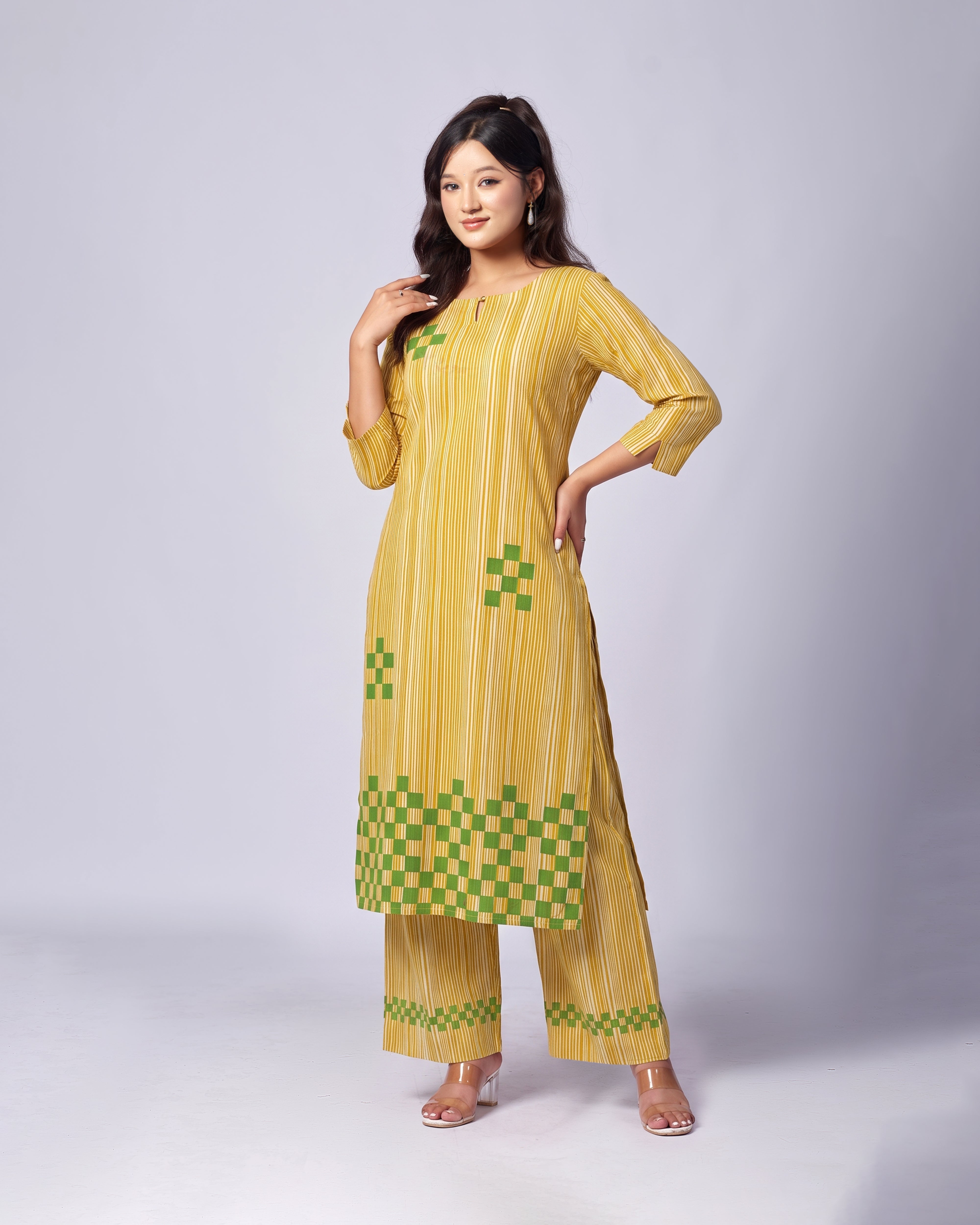 A woman modeling a yellow and green striped kurta set with matching wide-leg pants against a light gray studio background.